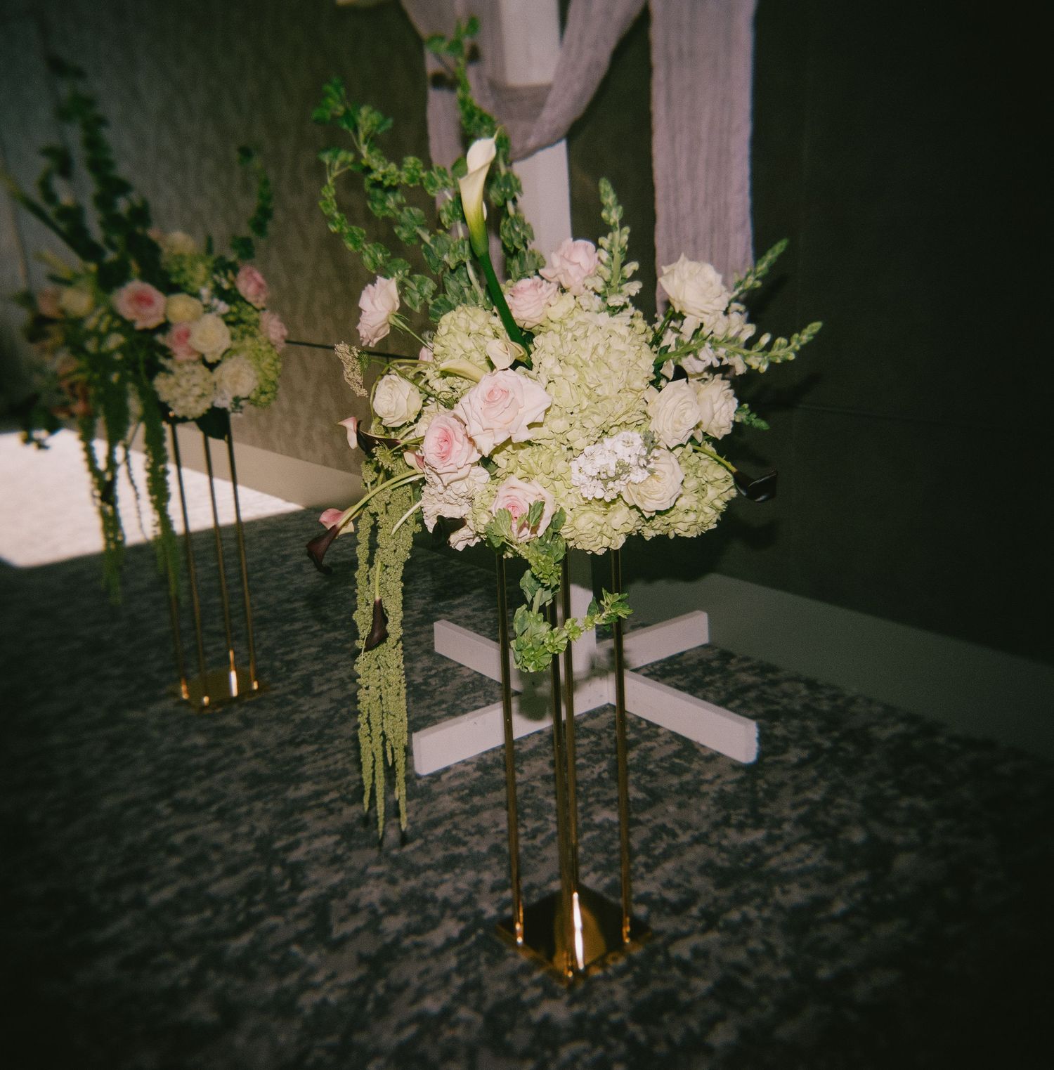 Romantic floral arrangement with pink and white blooms on gold stand at wedding reception.