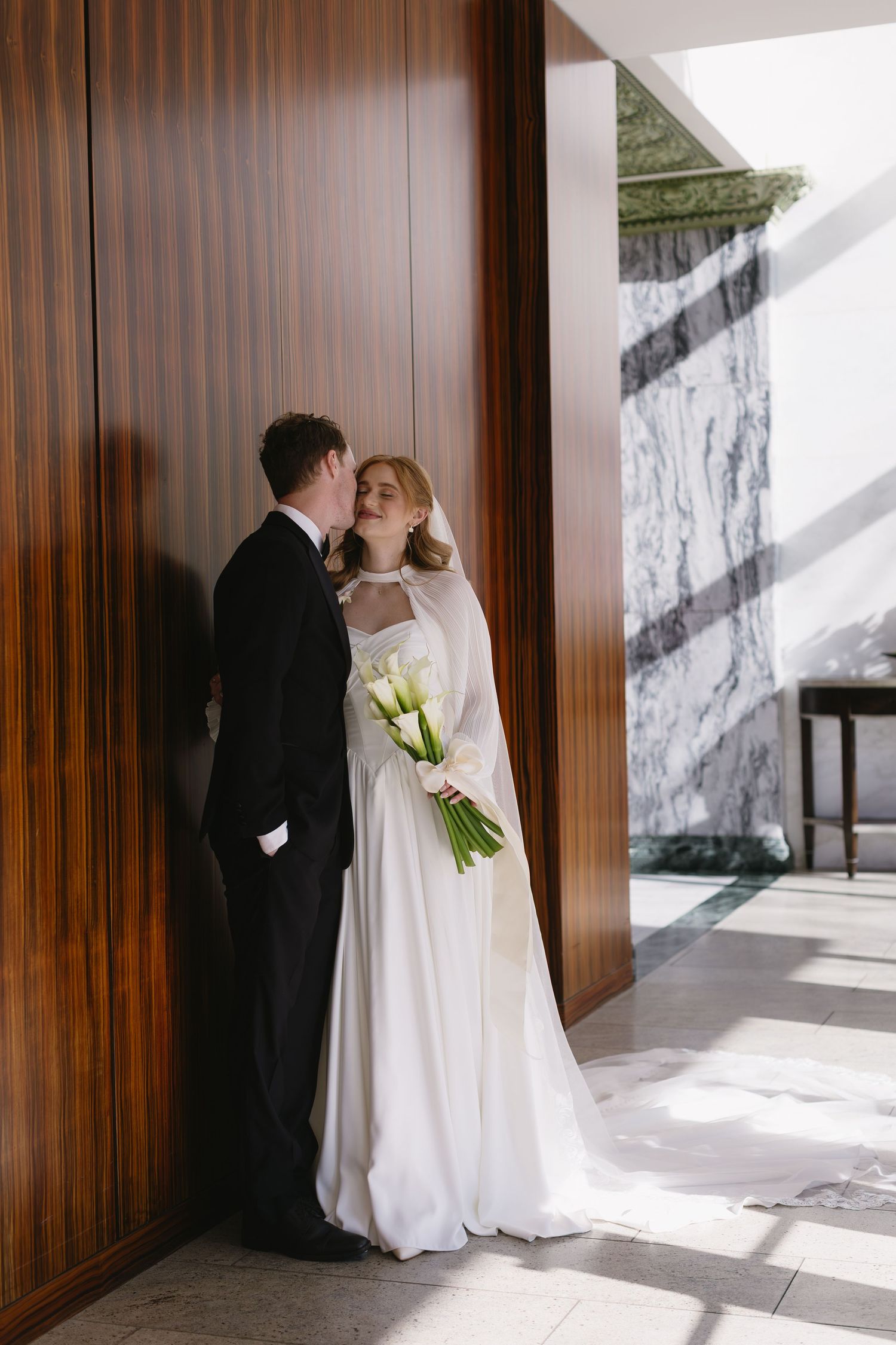 A romantic wedding moment captured against wooden paneled walls in natural lighting.