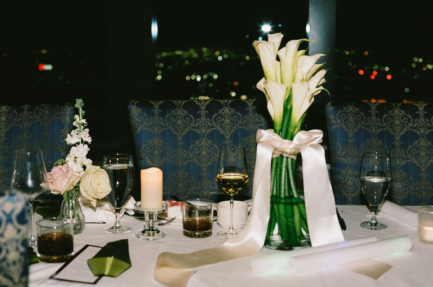 Elegant wedding reception table setting with white flowers in green vases and candlelight.