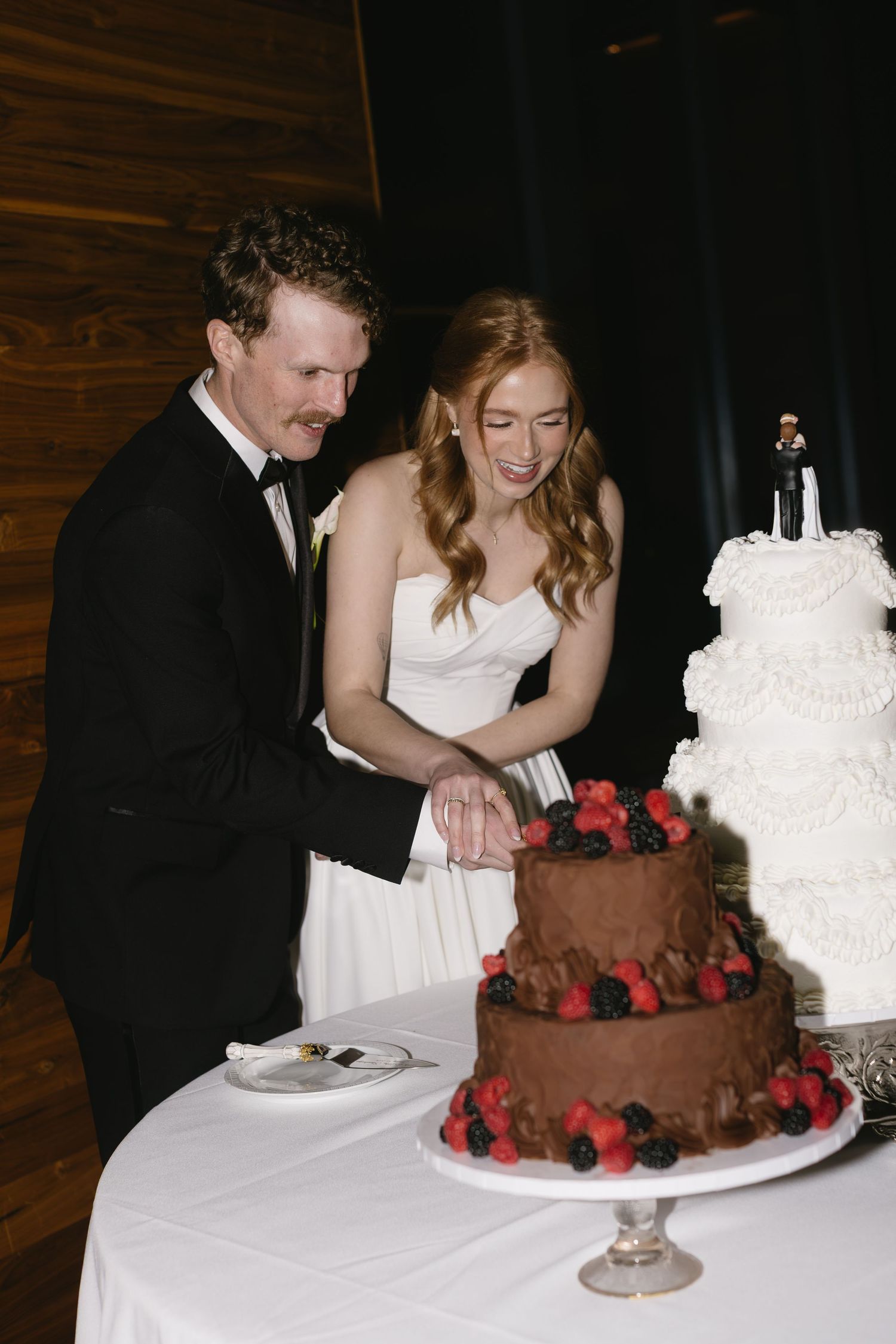 A wedding couple cutting into chocolate and white tiered cakes at their reception.