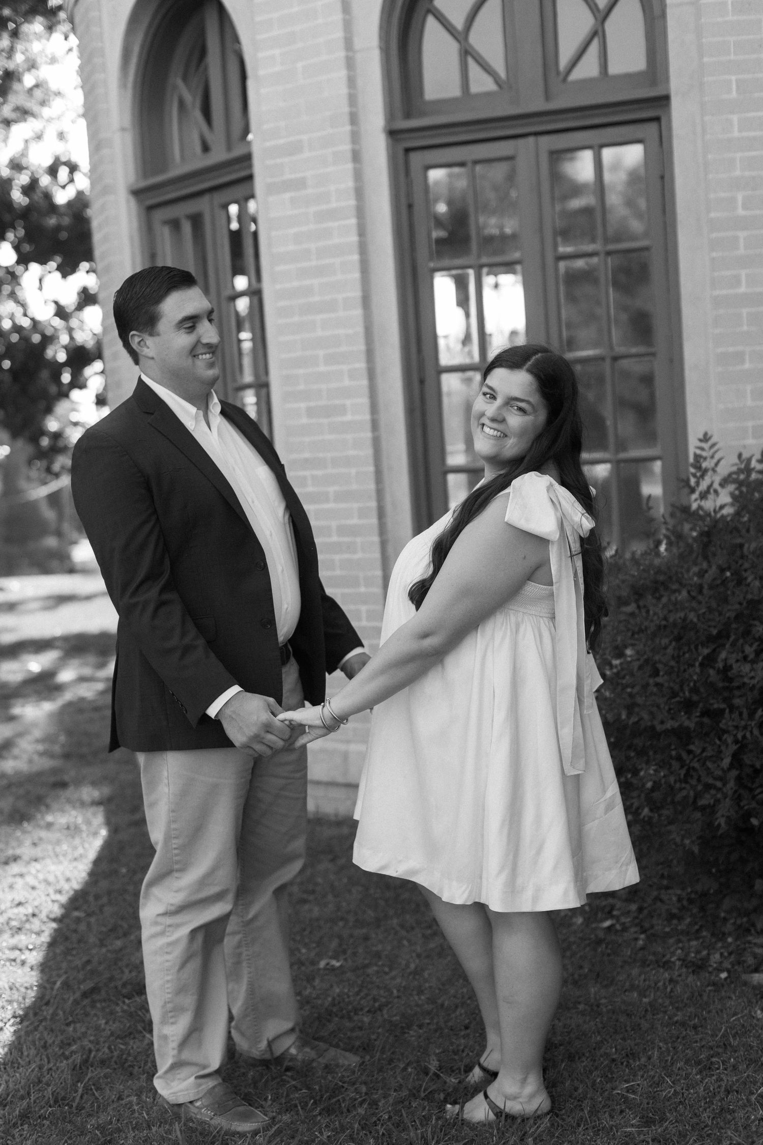 Black and white portrait of a couple holding hands by an arched doorway.
