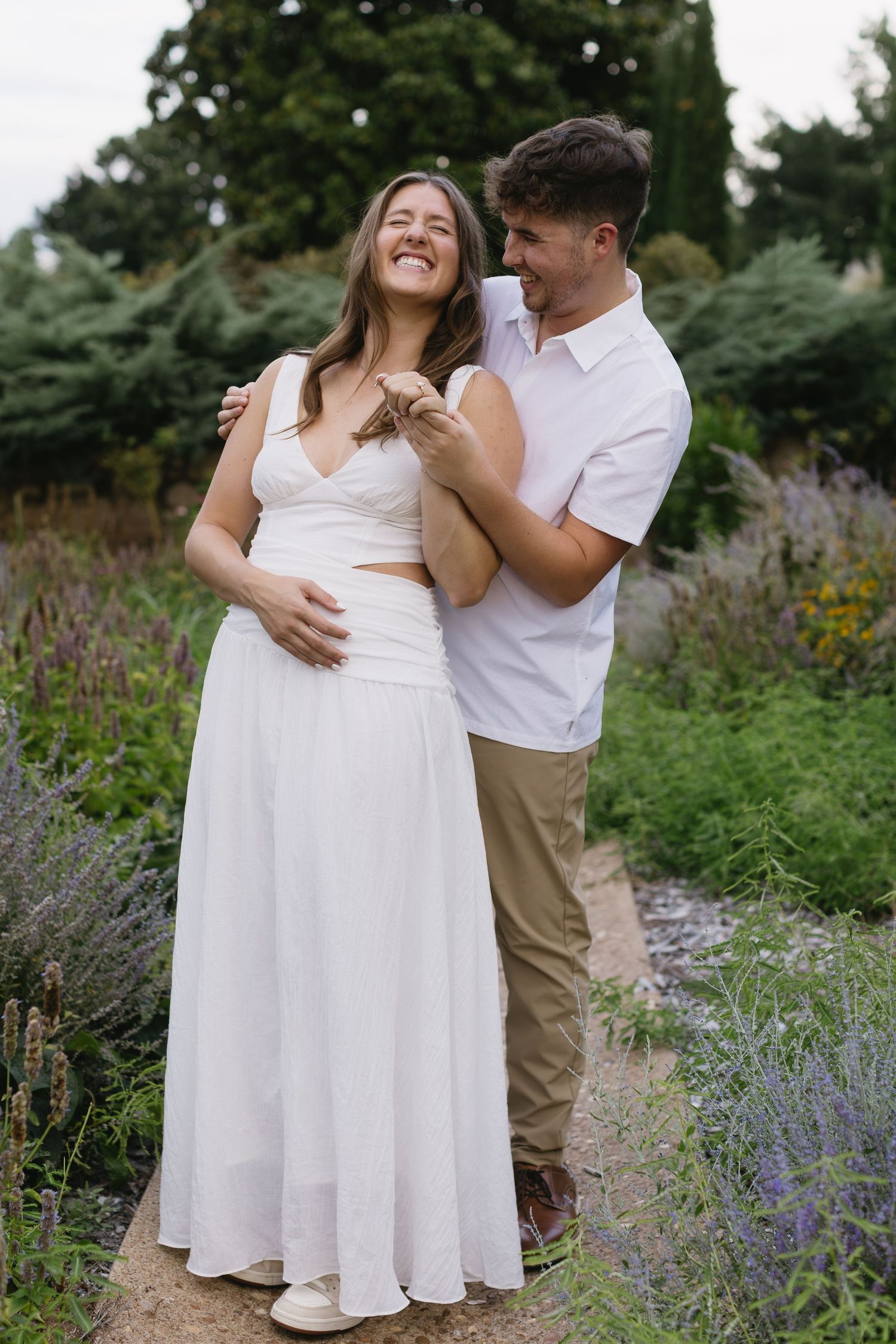 A couple shares a candid laughing moment together in a garden with lavender flowers.