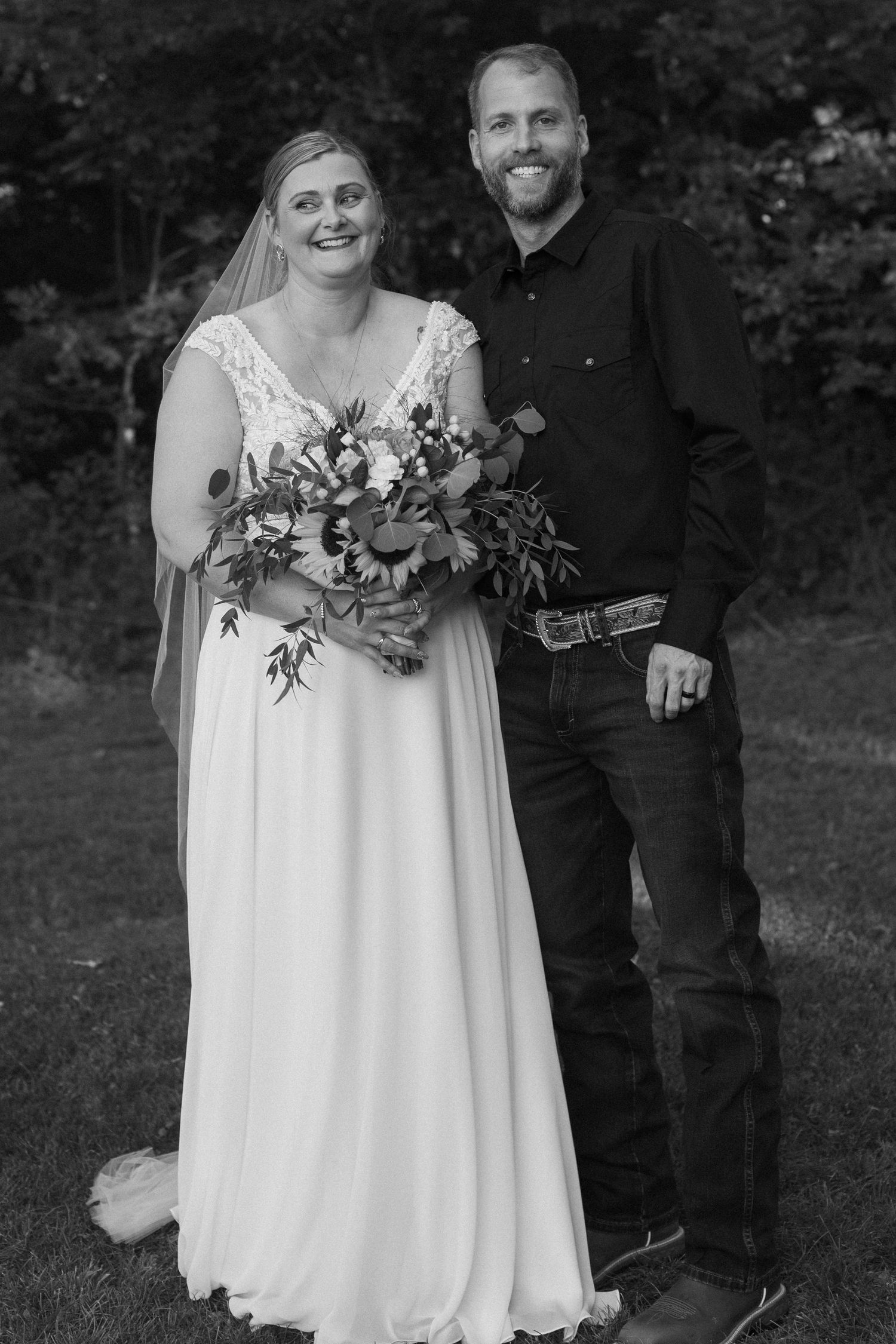 Wedding couple poses with floral bouquet in outdoor garden setting.