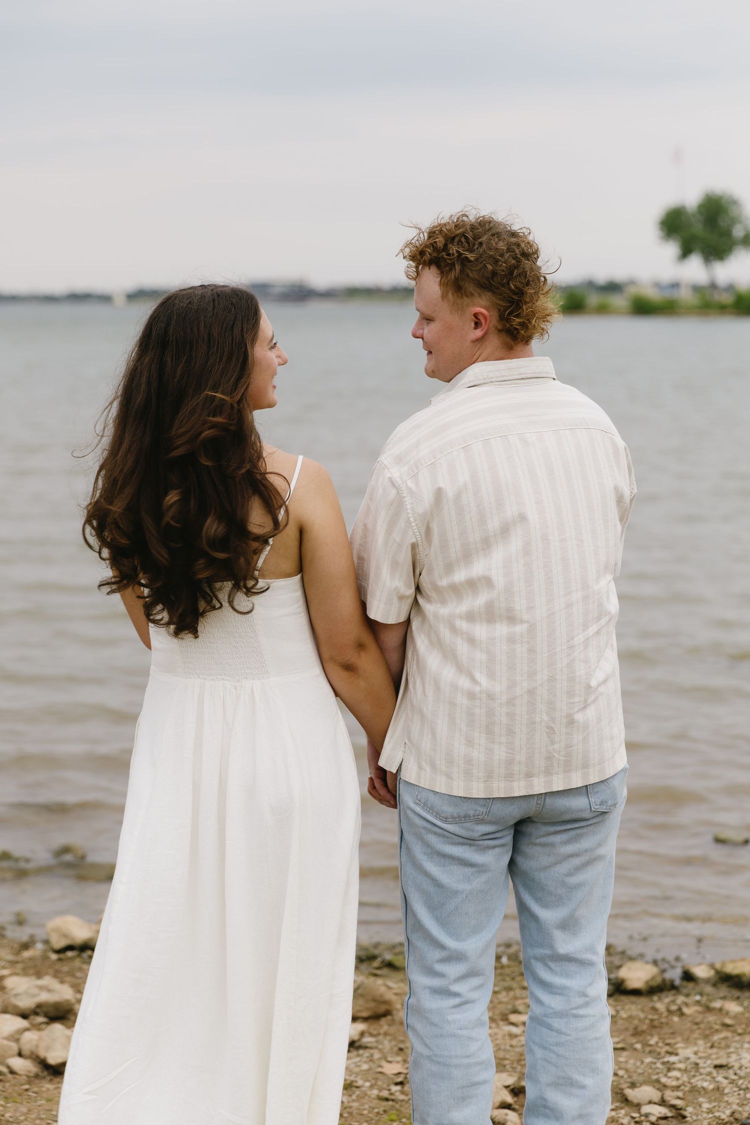 Couple wearing white stands together against scenic lake view.