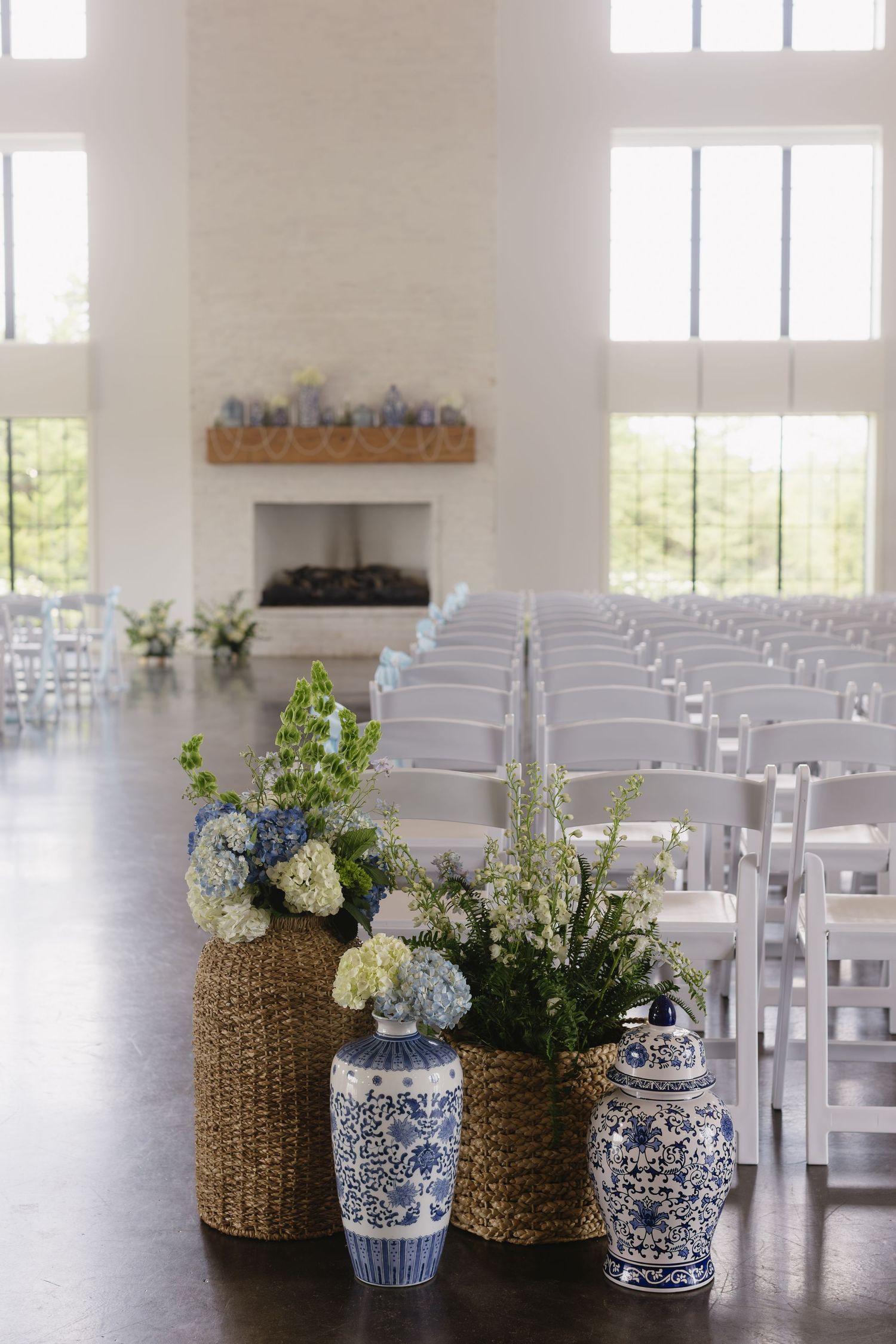 A bright wedding ceremony venue with white chairs and blue and white floral arrangements in ceramic vases.