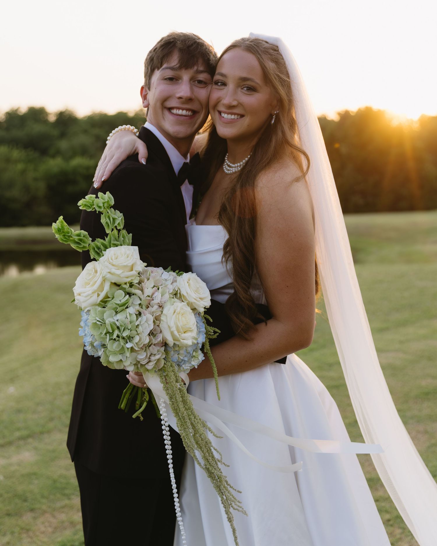 Romantic sunset wedding portrait with white bouquet and flowing veil.
