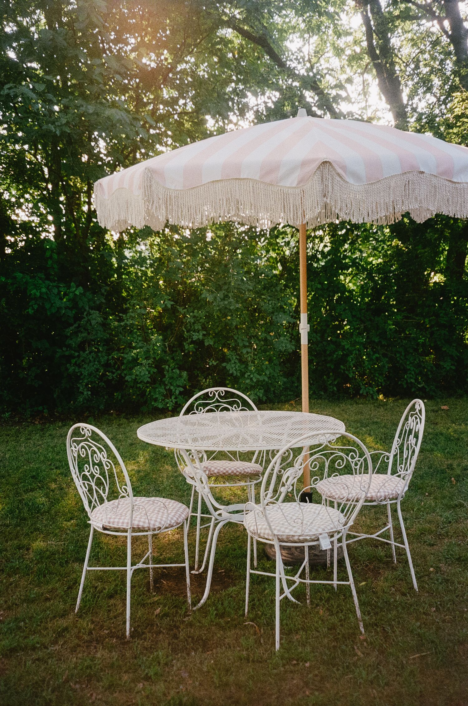 Vintage white garden furniture with parasols arranged on a lawn in evening sunlight.
