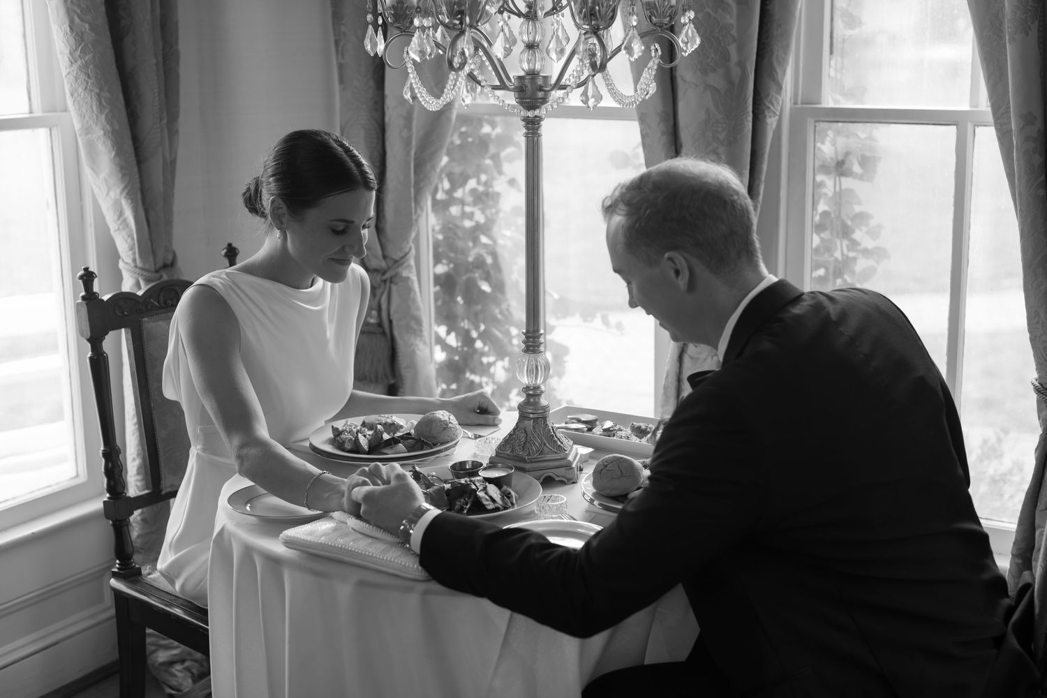 A formal dining scene in black and white showing a couple having an intimate meal by a window.