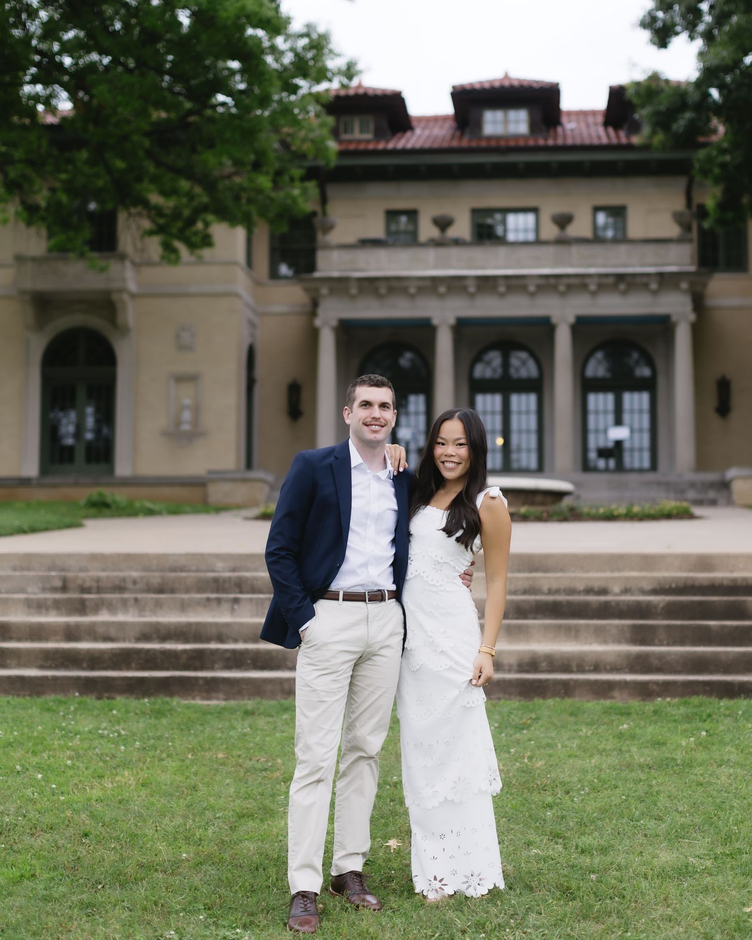 Couple embraces on stone steps at a grand historic building in matching white and navy outfits.