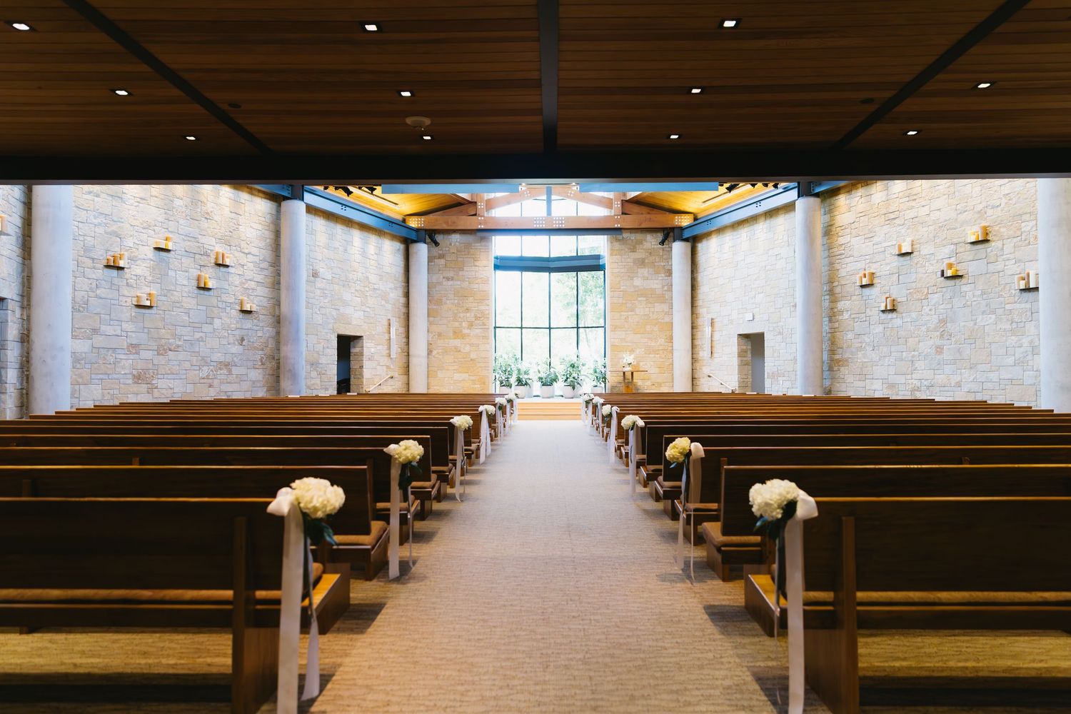 Interior view of a modern stone church sanctuary with wooden pews and large windows illuminating the worship space.