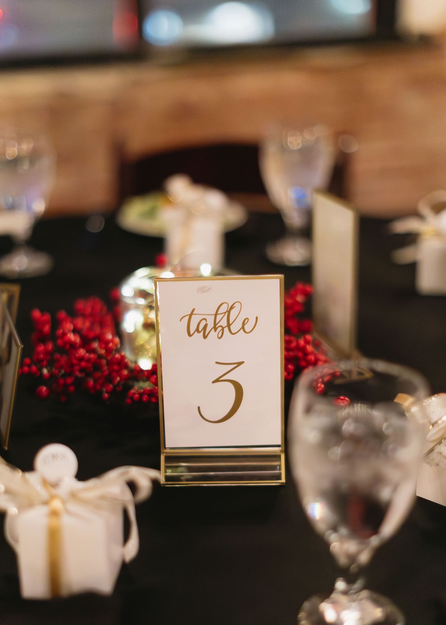 Elegant gold table number cards with red berries decorate a formal dining setting.