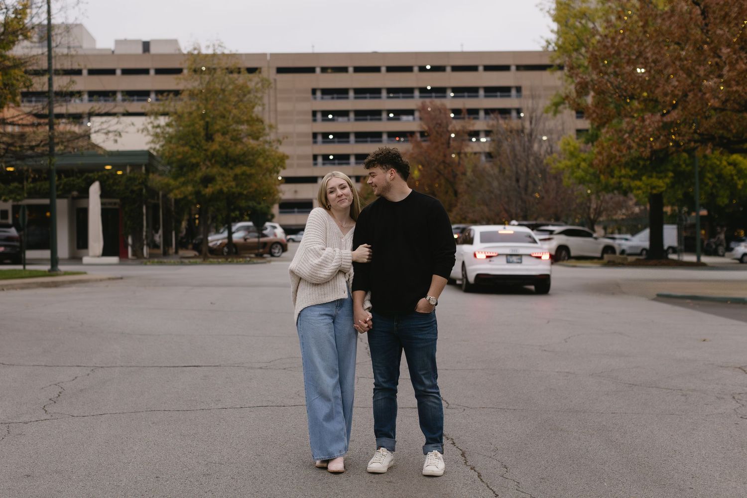 A couple strolls casually through an urban parking area on an autumn day.