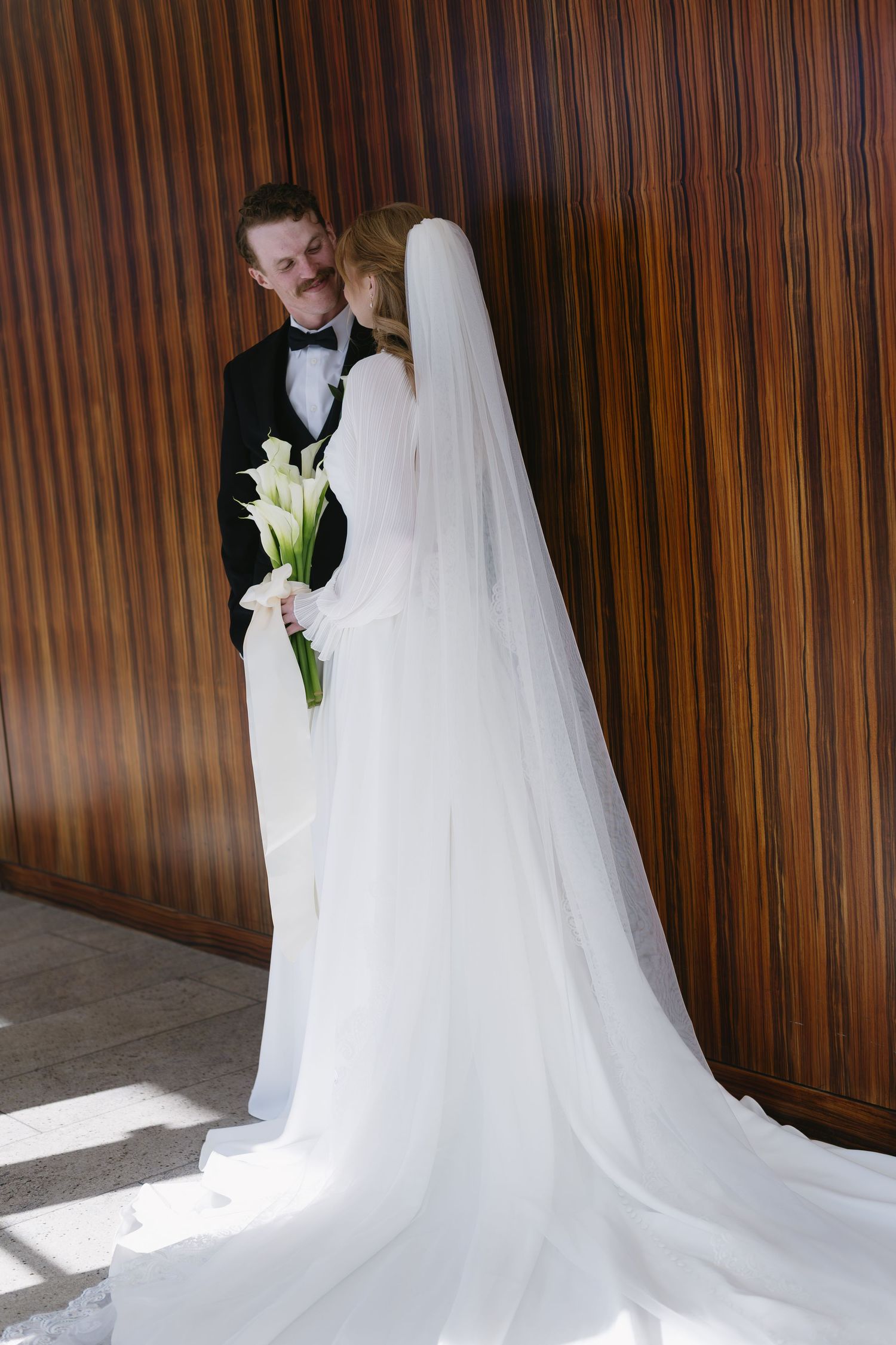 A flowing white wedding dress with long train photographed against dark wood paneling.