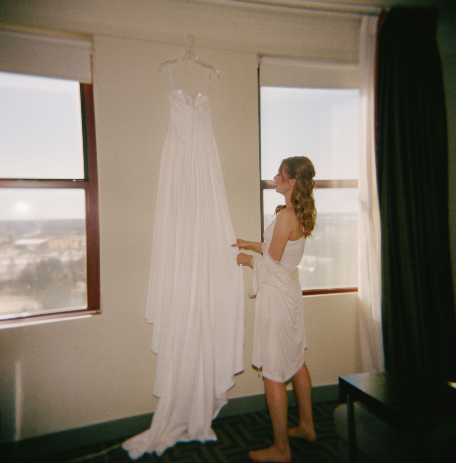 Wedding dress and accessories hanging by a window in morning light.