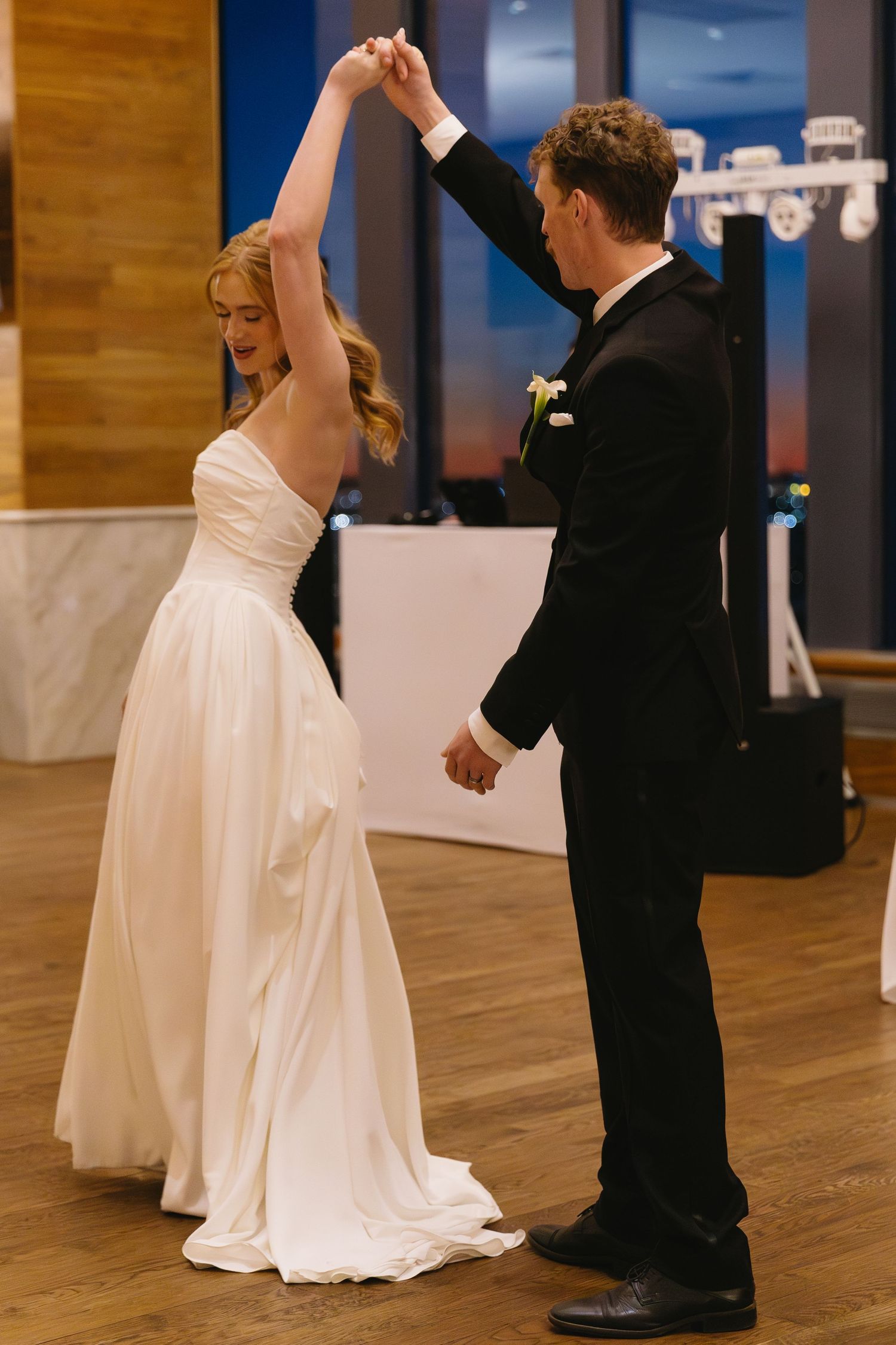 Bride and groom dancing together on wooden floor during wedding reception.