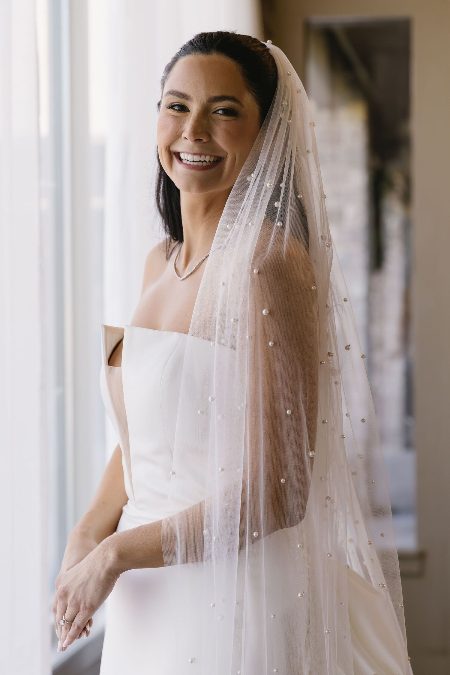 Elegant bride wearing a pearl-studded veil in natural window light.