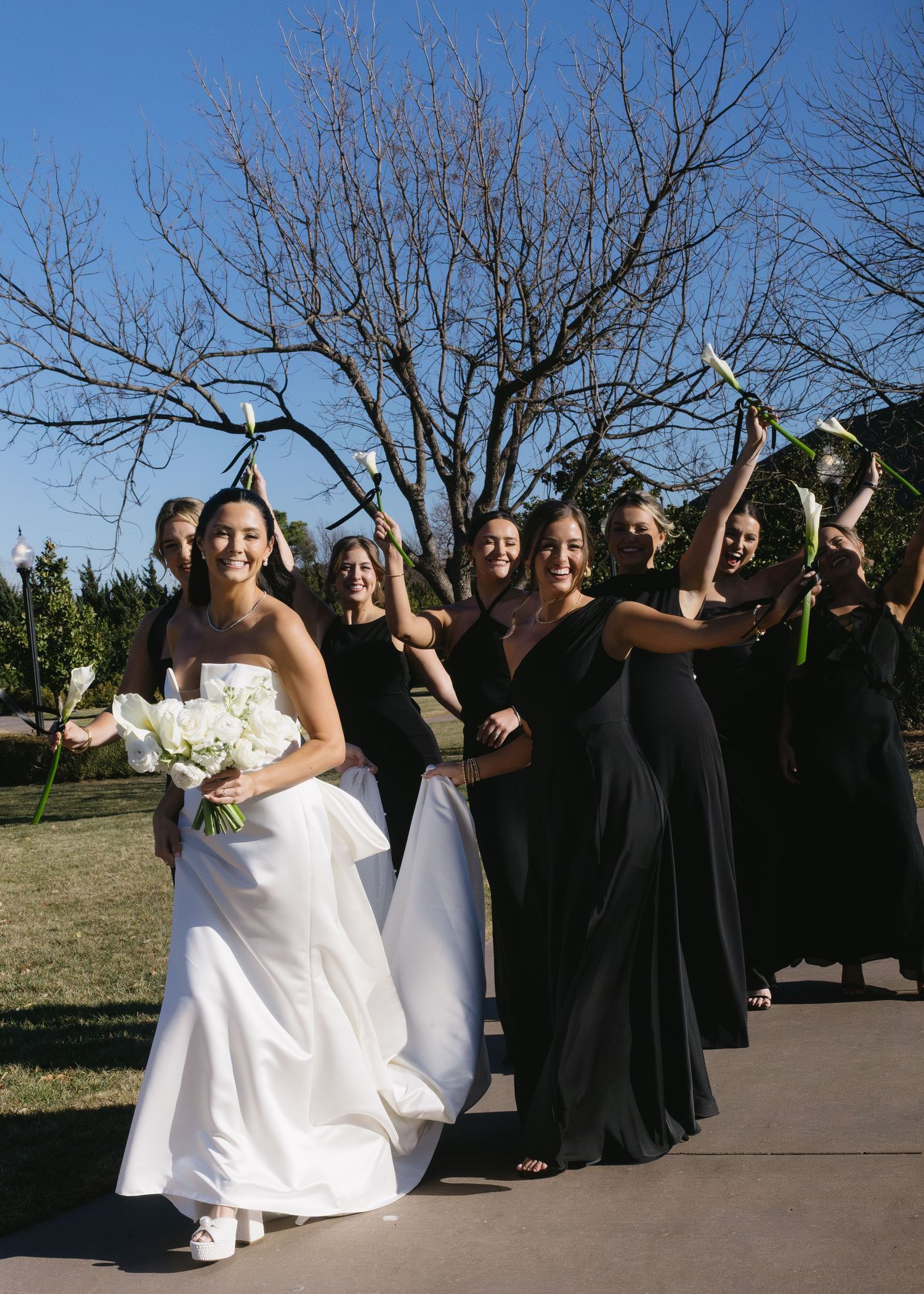 Wedding party in black and white attire posing outdoors against a blue sky.