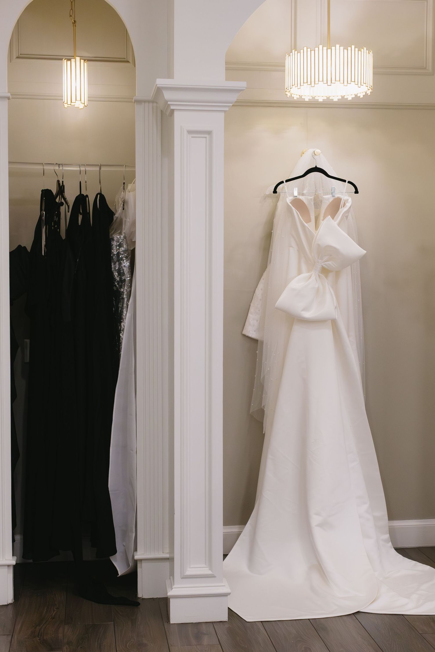 White wedding dresses displayed on hangers in an elegant bridal boutique with modern lighting fixtures.