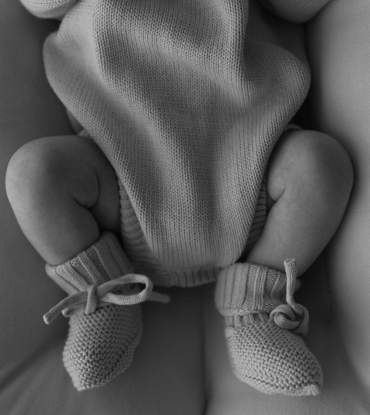 Artistic black and white close-up of baby feet in knitted booties.
