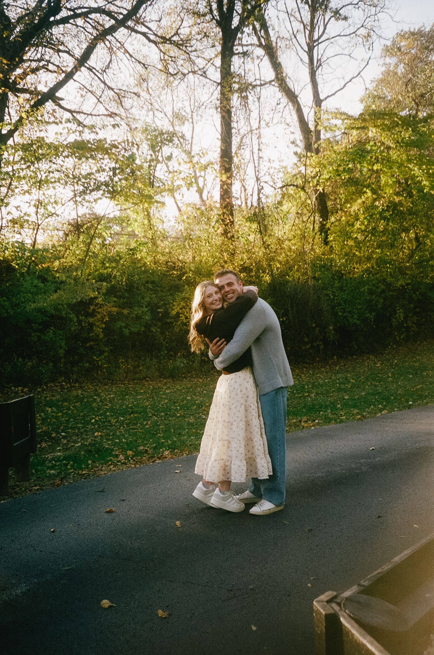 A romantic couple embraces on a tree-lined path during an autumn engagement photoshoot.
