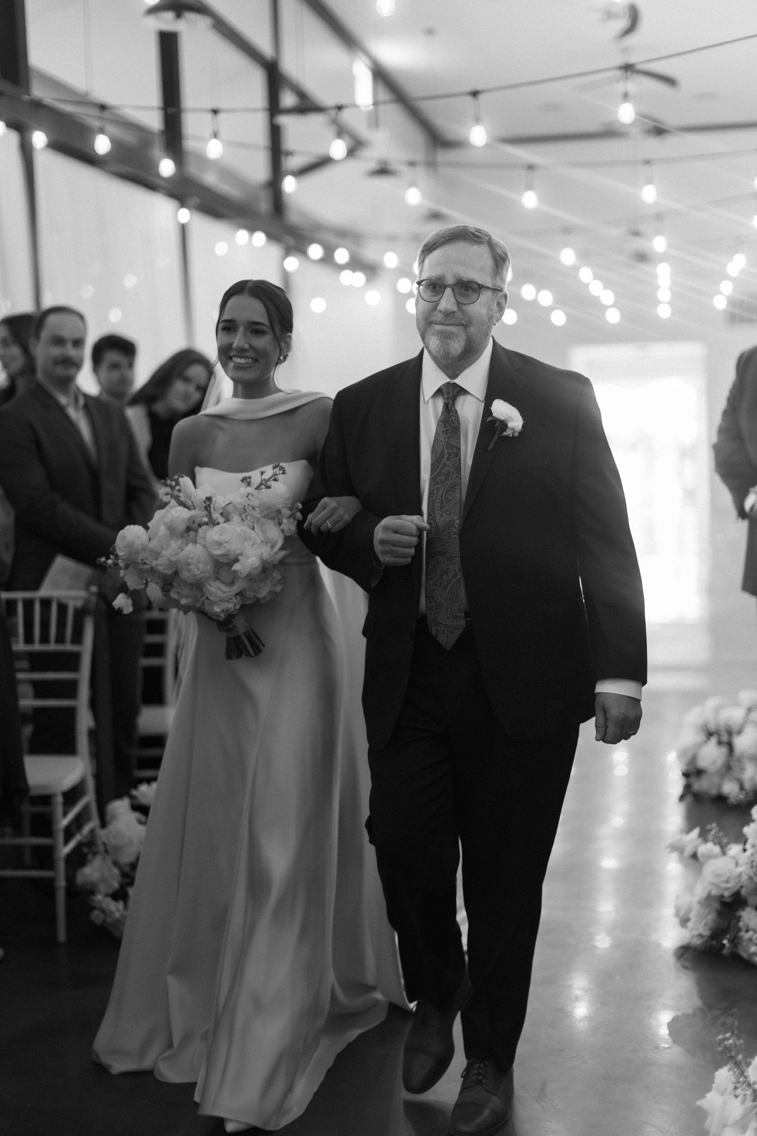 Wedding party walking down an elegant hallway decorated with string lights and floral arrangements.