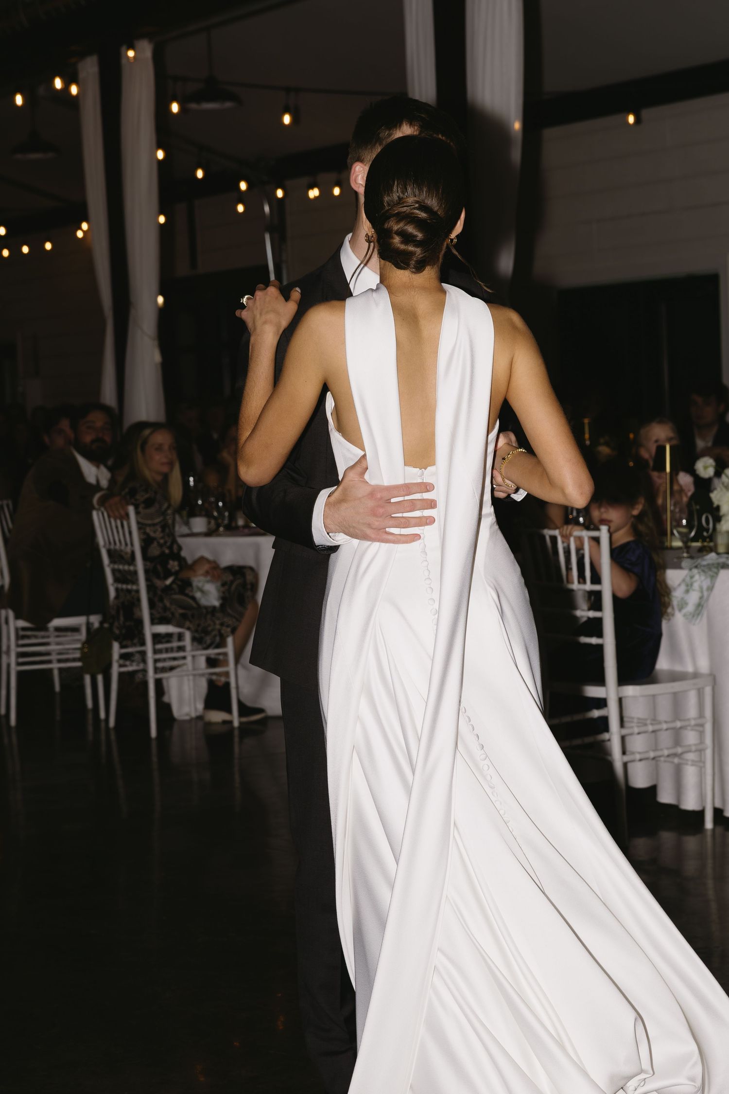 Back view of an elegant white wedding dress with open back design at an evening reception.
