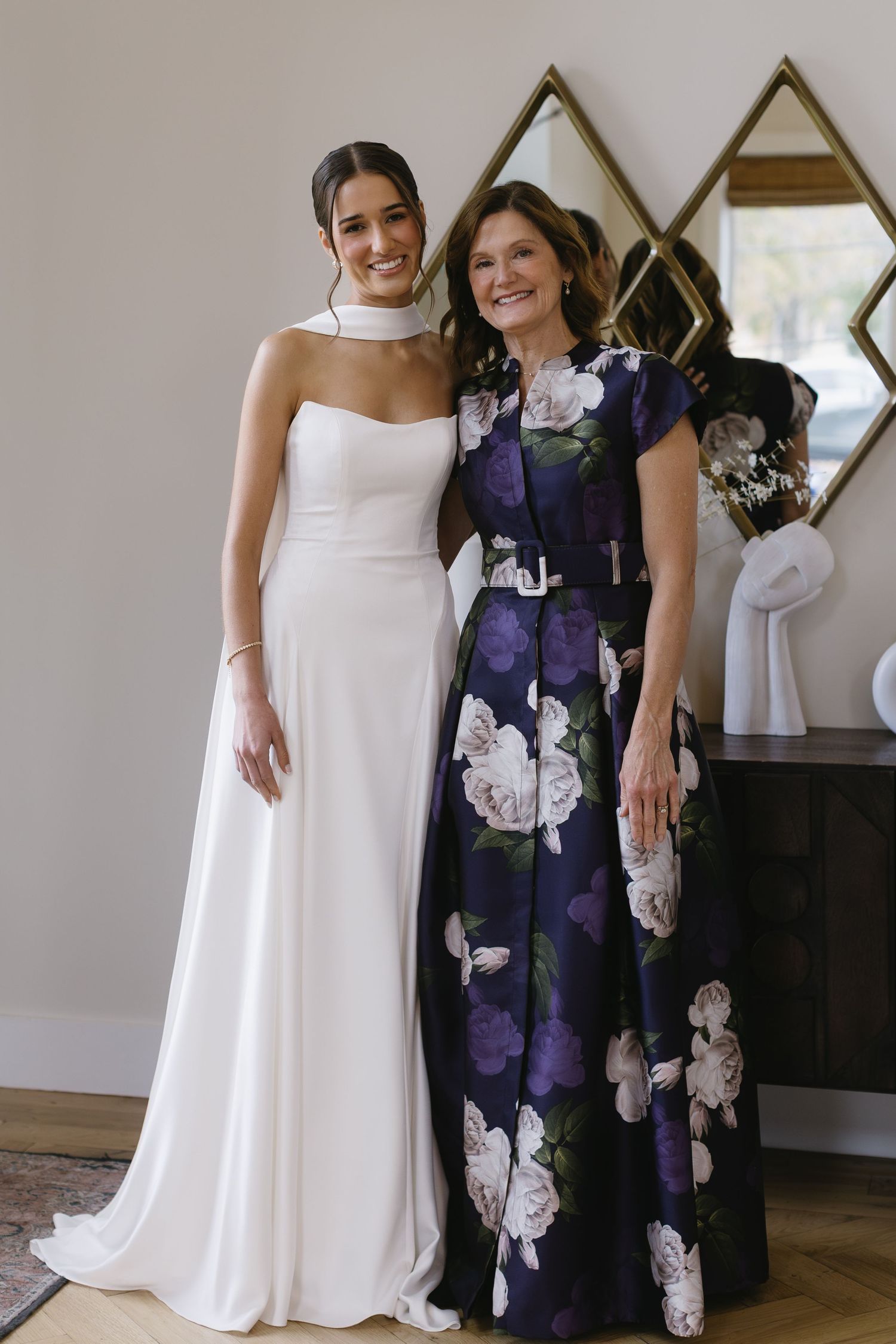 A wedding scene featuring an elegant white bridal gown and navy floral dress against geometric wall decor.