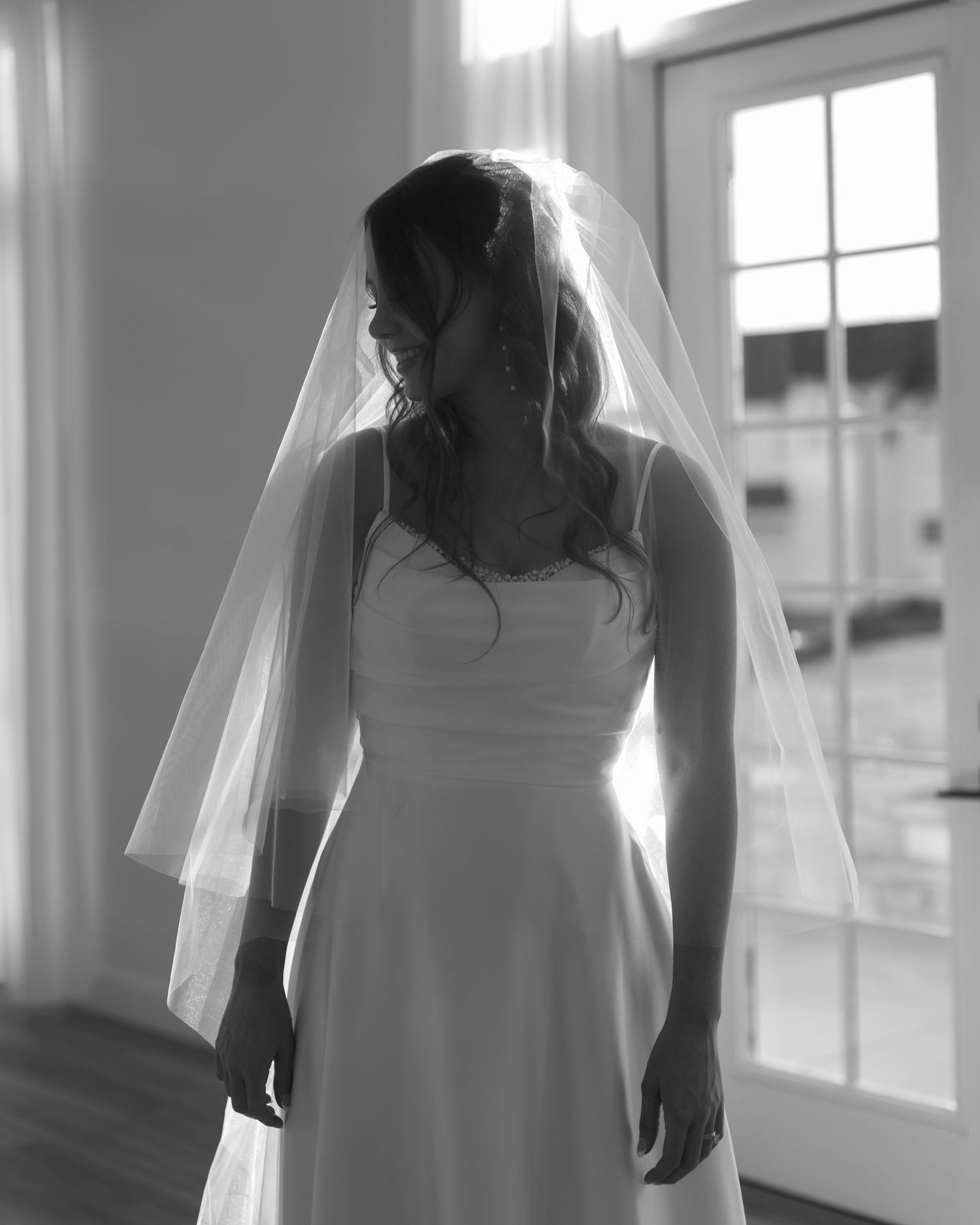 Silhouetted figures in white wedding dresses stand in sunlit hallway creating an ethereal effect.