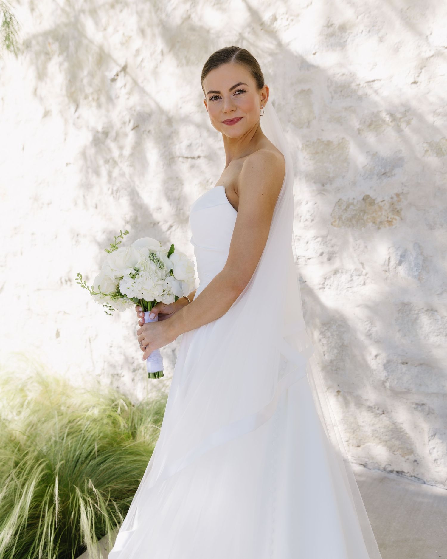 Elegant bridal portrait against a white stone wall with a classic bouquet.