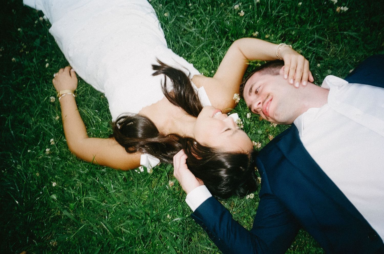 Playful couple's photoshoot with subjects laying in green grass during summer.
