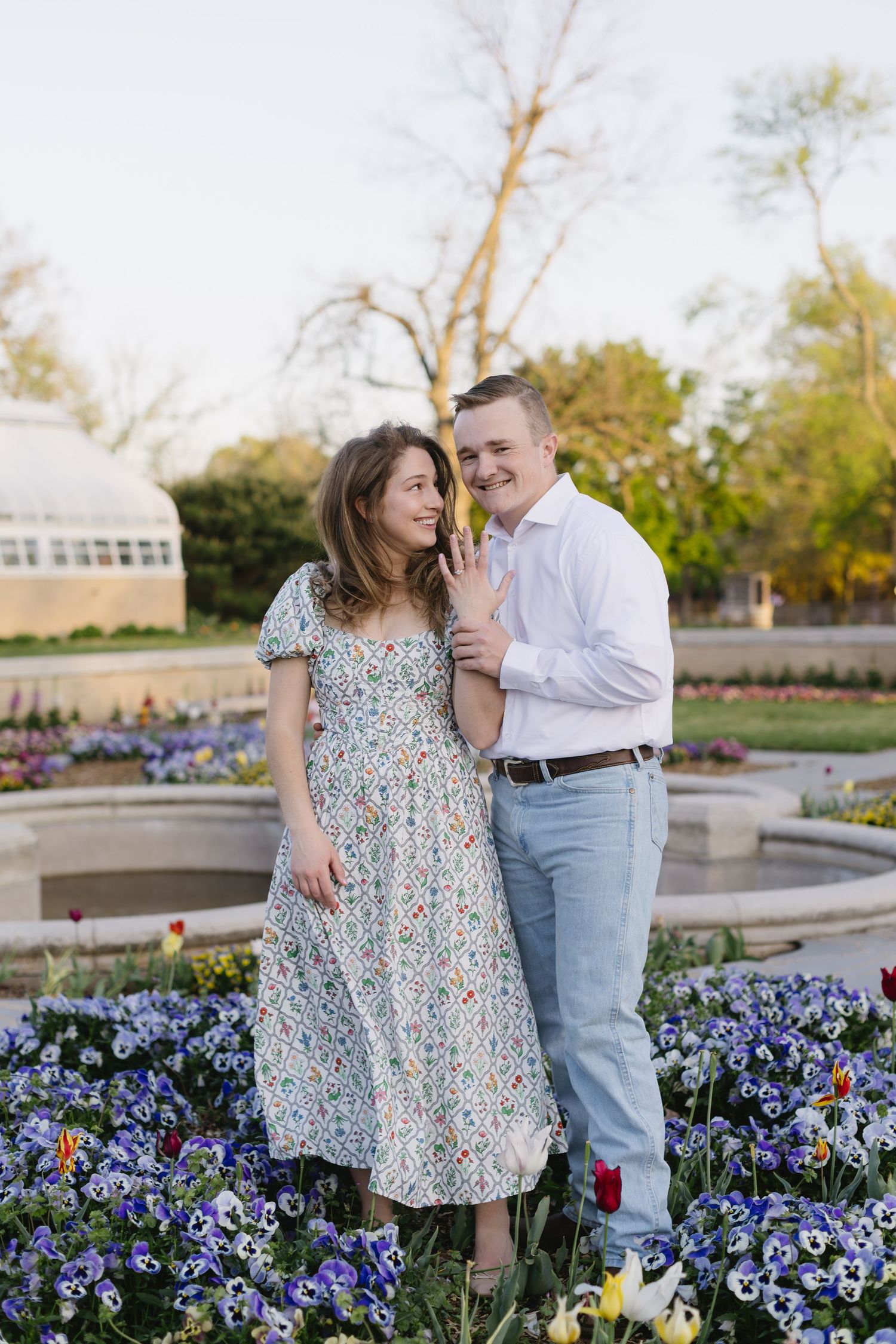 A couple embraces among beautiful purple flowers in a garden courtyard during springtime.