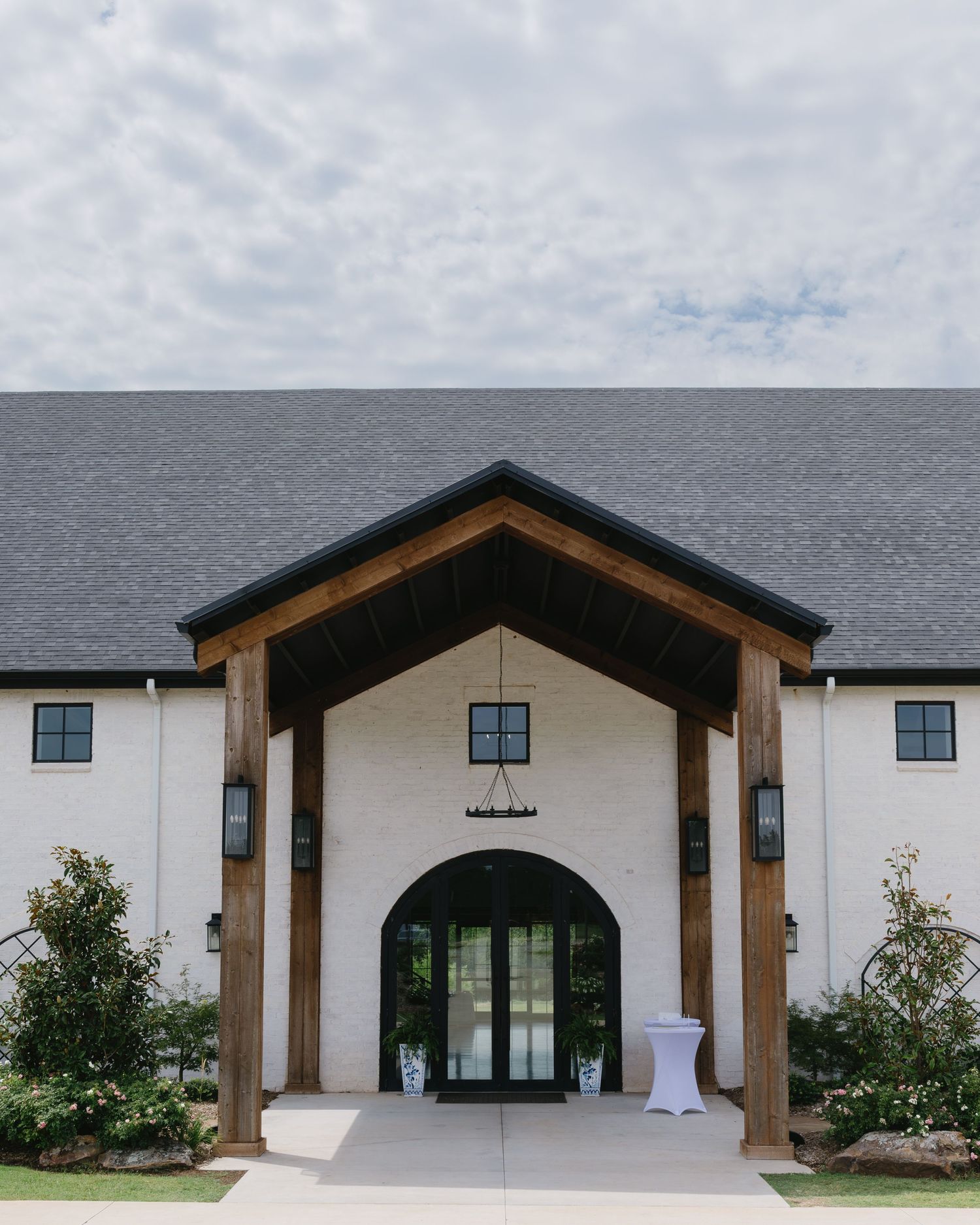 Modern white wedding venue exterior with wooden beam accents and arched doorways.