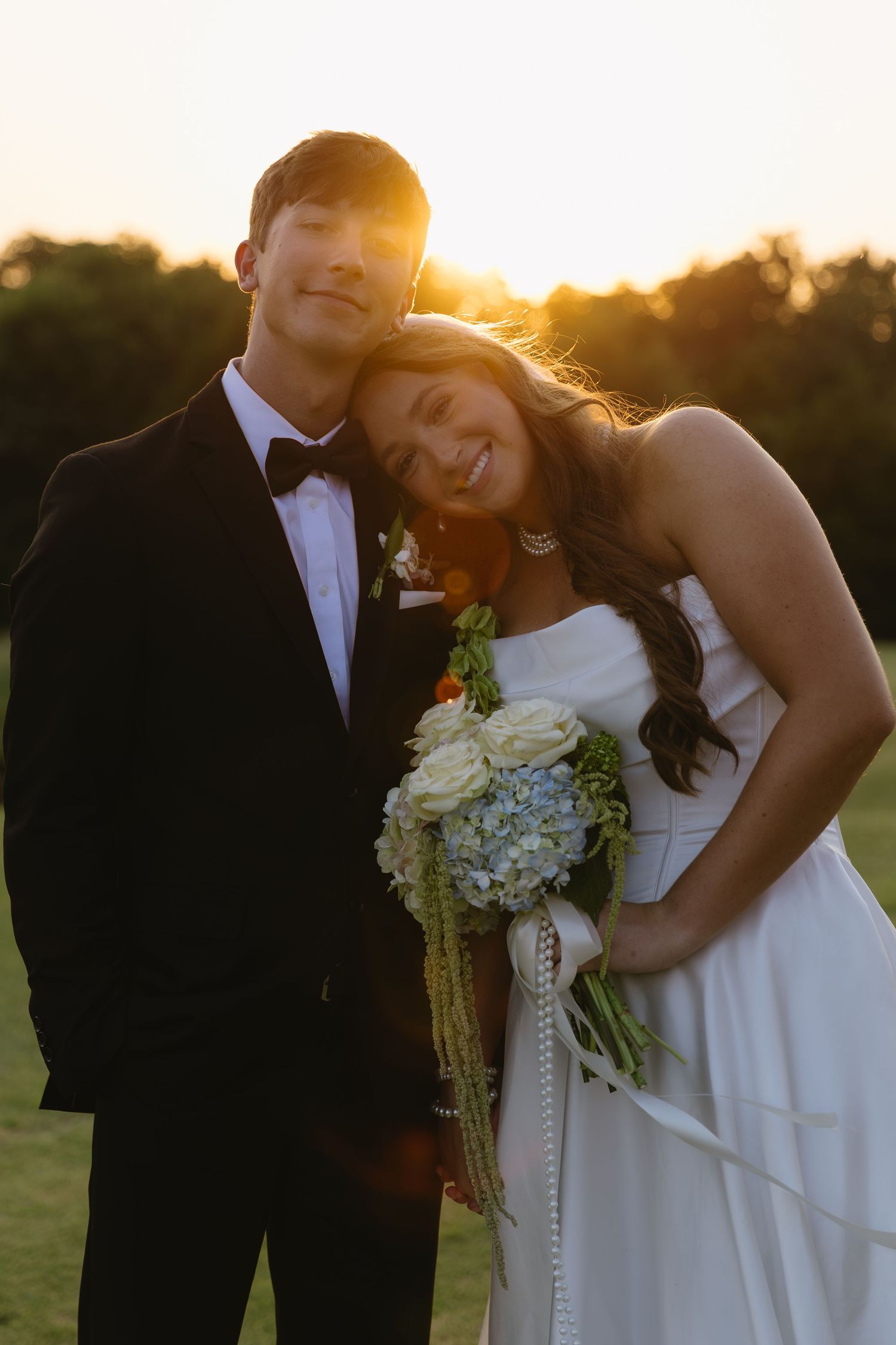 Romantic sunset wedding photos with couple embracing on grassy field.