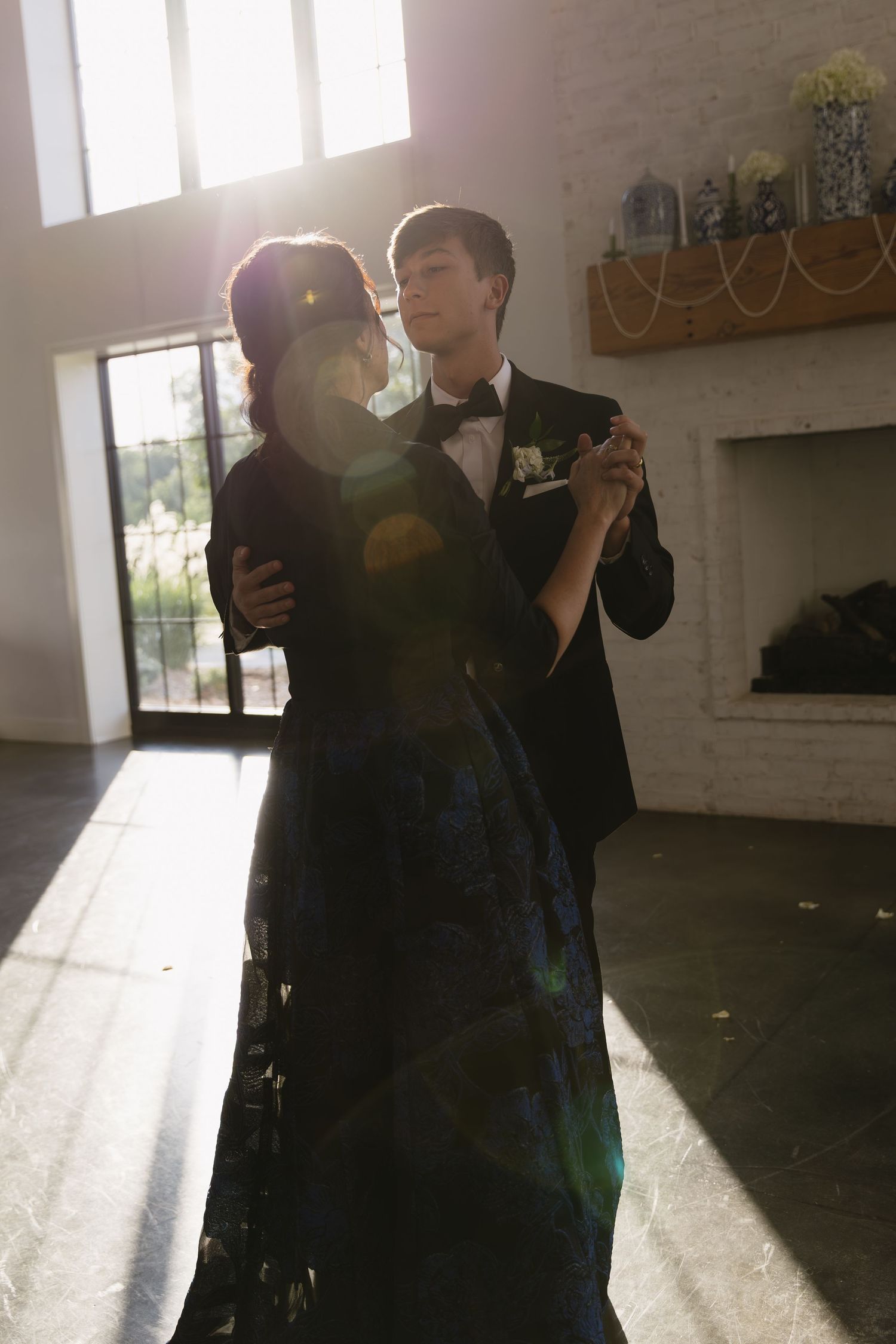 A couple dancing in a sunlit indoor space with wooden floors and large windows.