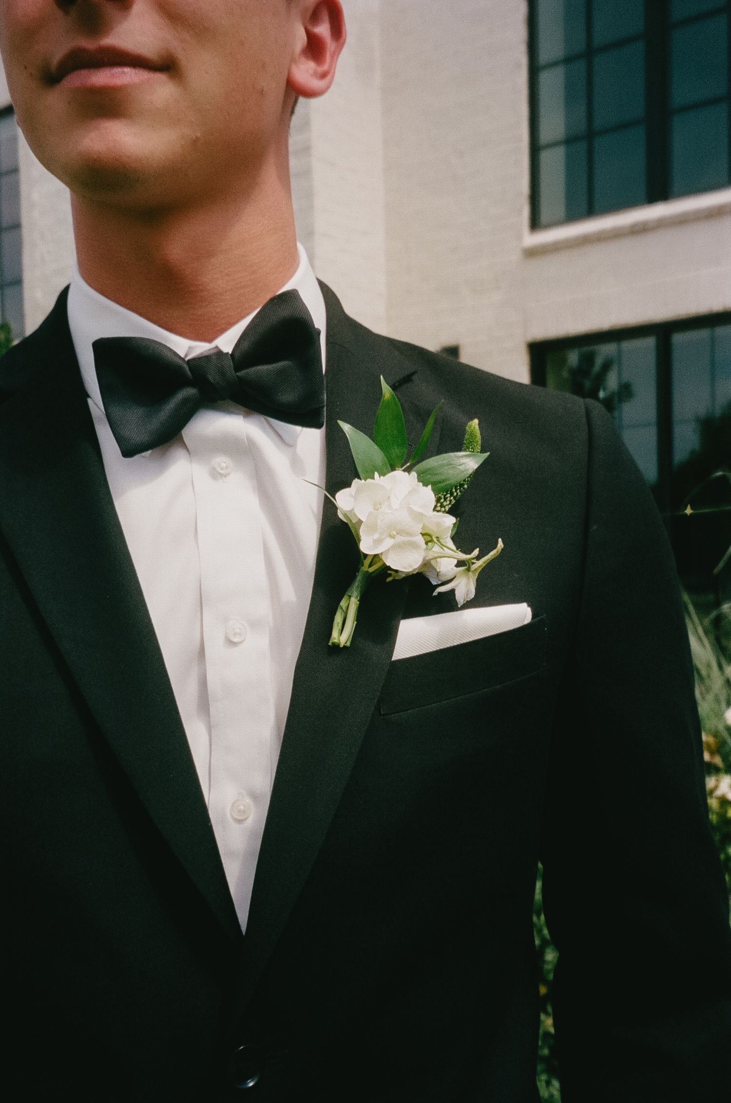 Close-up detail shots of a groom's black tuxedo with white boutonnière.