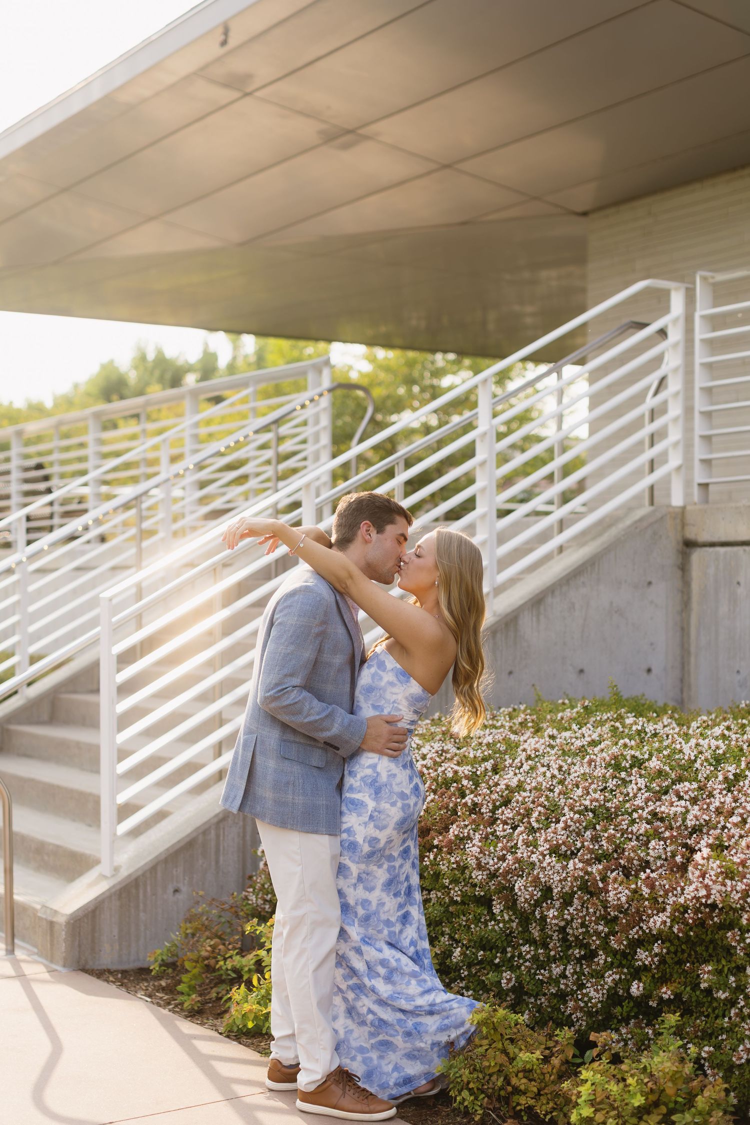 Romantic moment captured on concrete steps with white railings and landscaping.