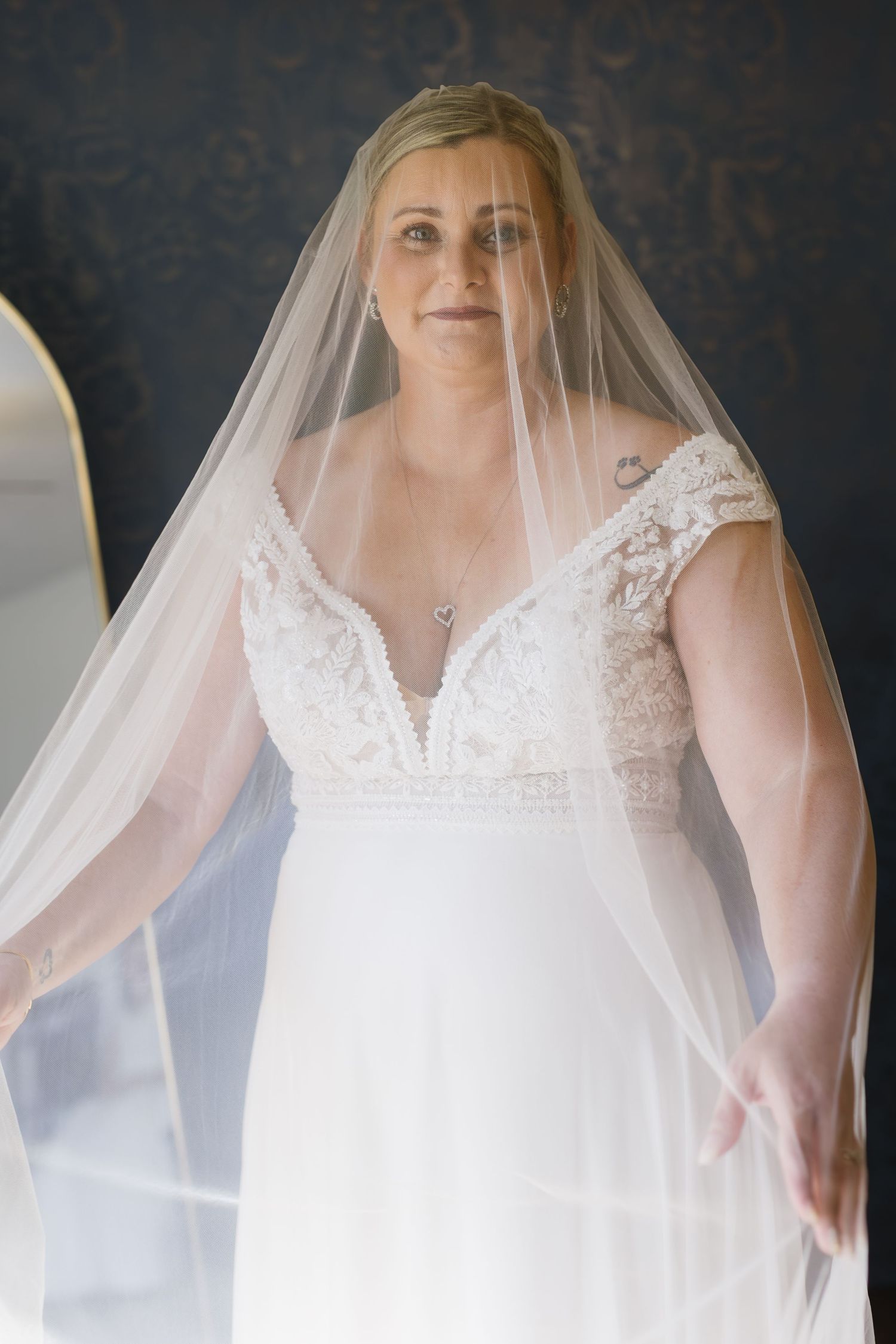 A flowing white wedding dress with delicate lace details and a sheer veil photographed against a dark background.