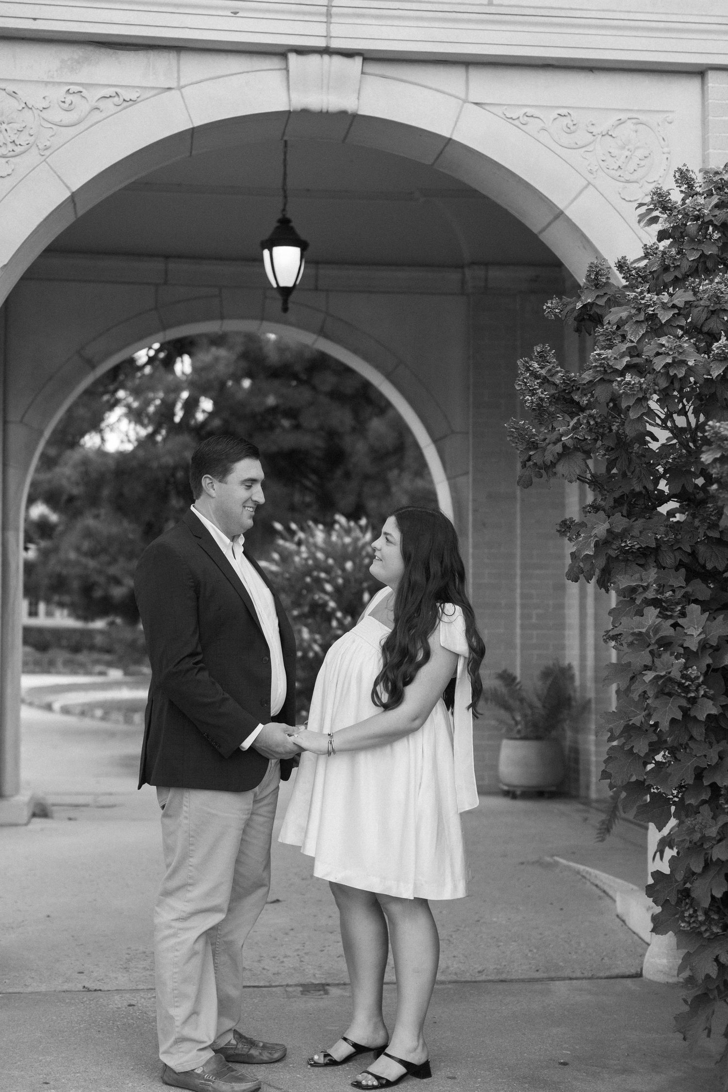 A black and white photo series of a couple posing playfully under a stone colonnade.