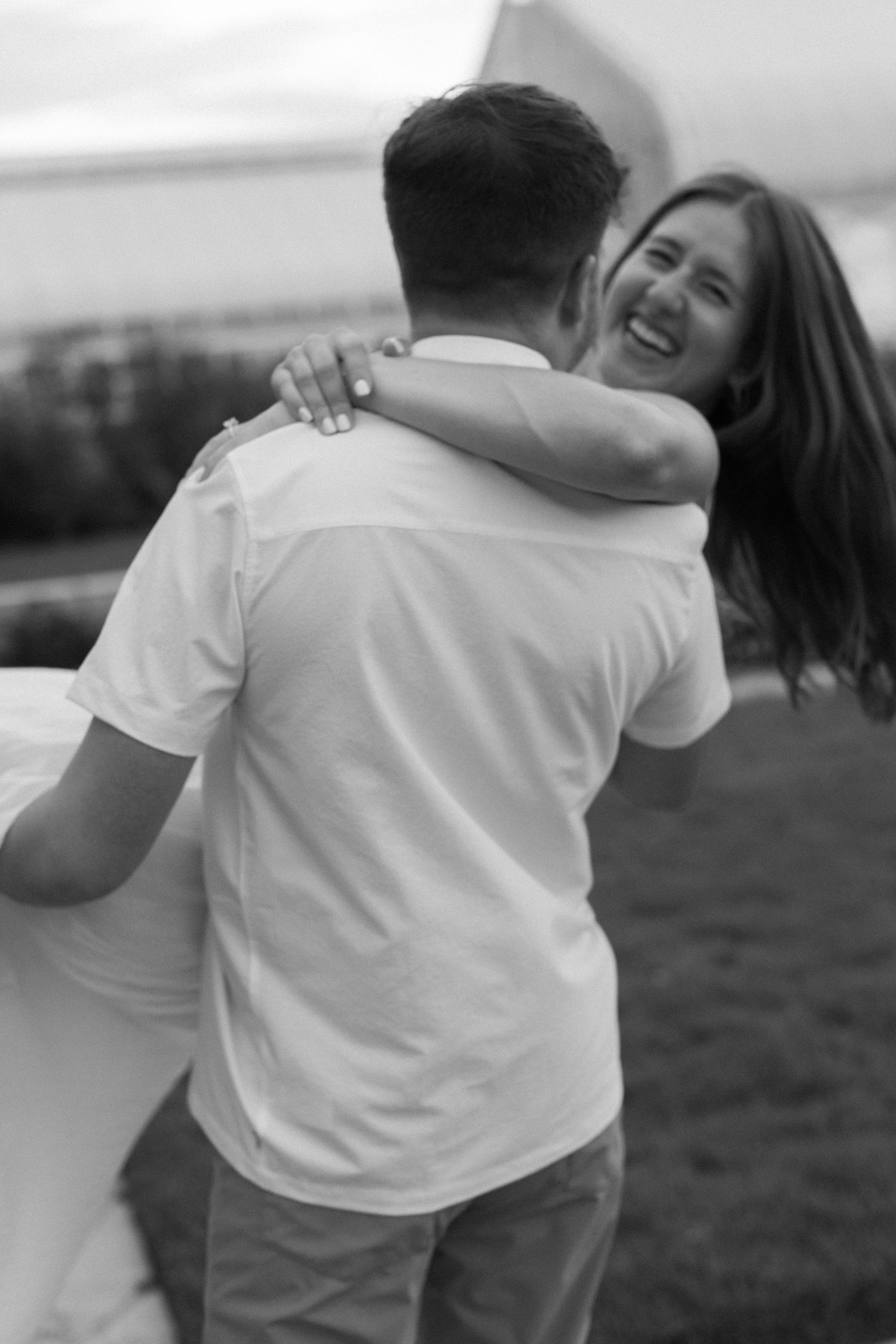A romantic black and white photo of a couple embracing outdoors with wind blowing through their hair.