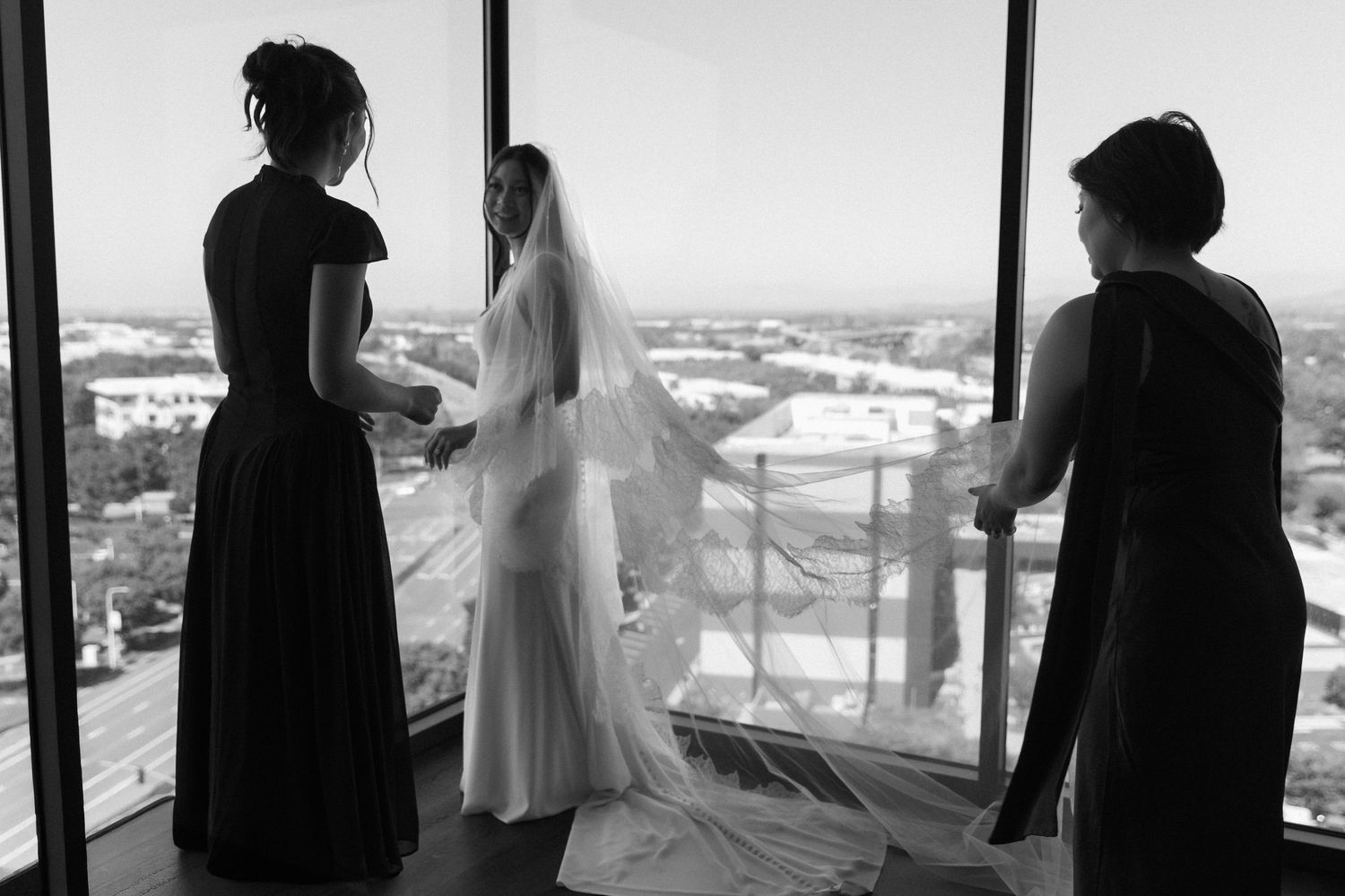 Silhouettes of a wedding party against large windows with a cityscape view.