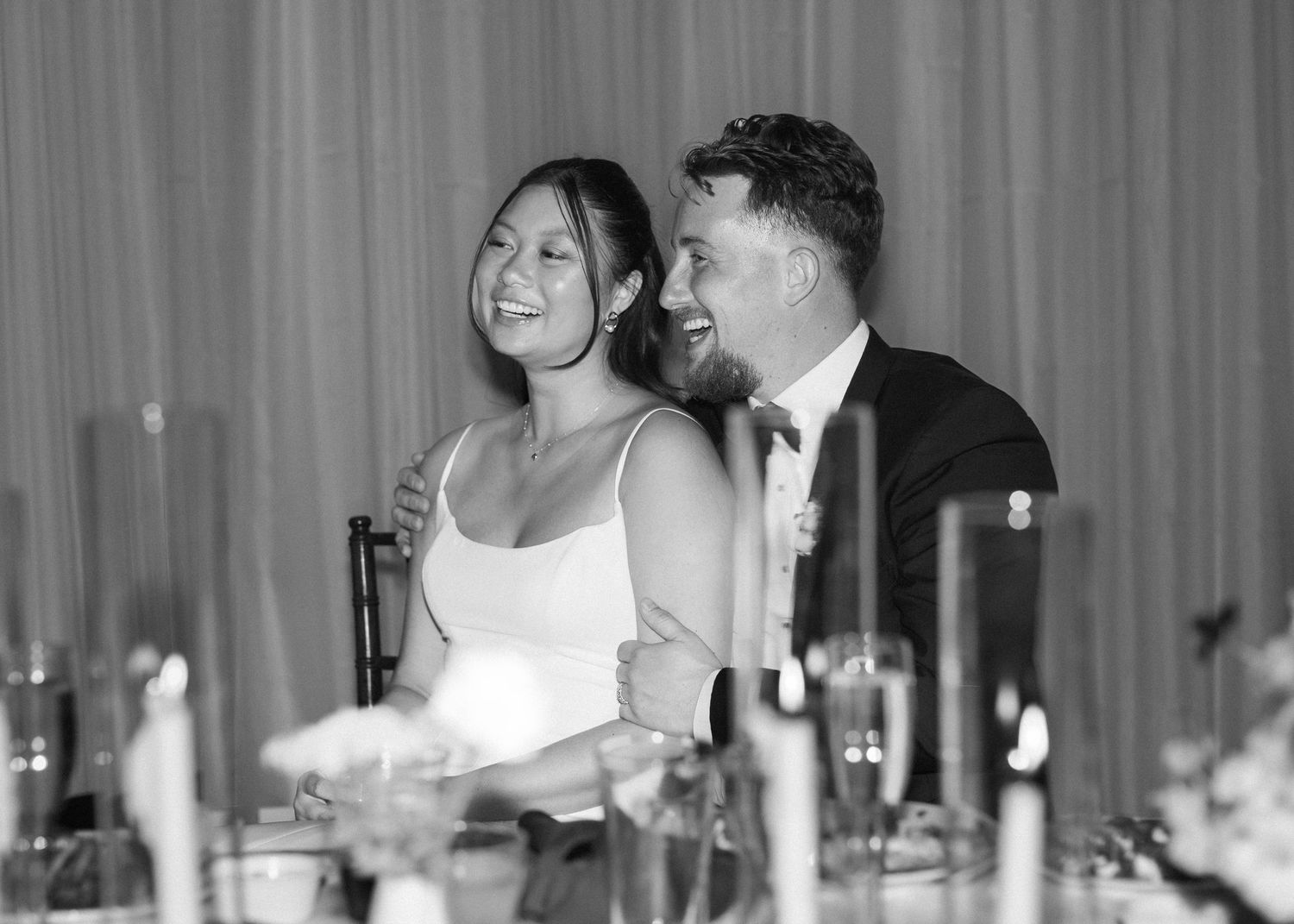 Black and white reception photo showing guests enjoying dinner at elegantly set tables.