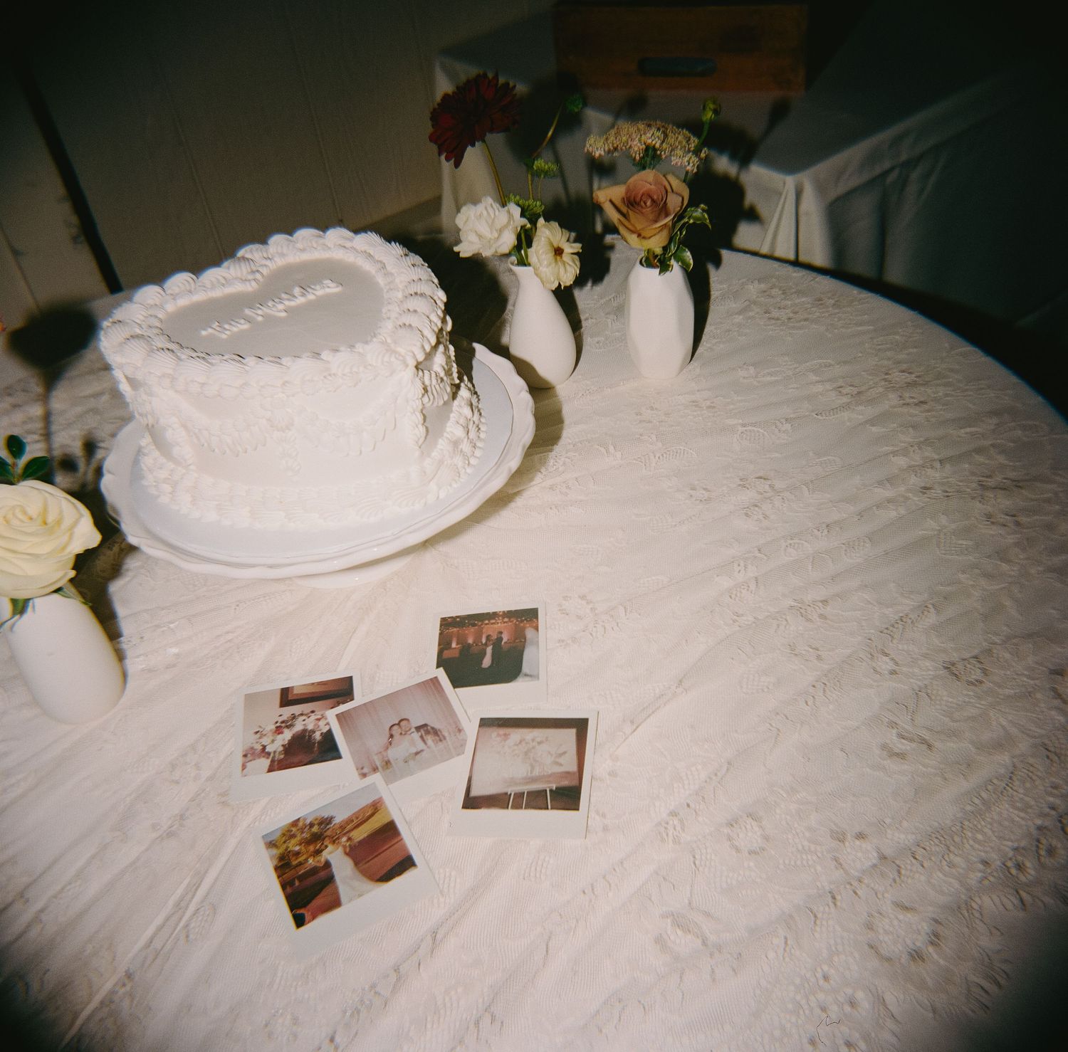 Vintage photographs scattered on a white tablecloth next to delicate floral centerpieces at a wedding reception.