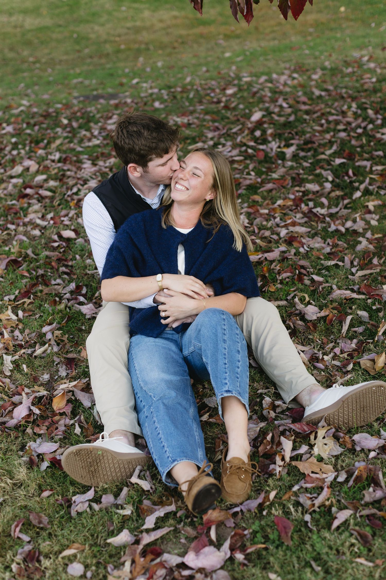 Couple sitting together on autumn leaves during outdoor photoshoot showing natural affection.