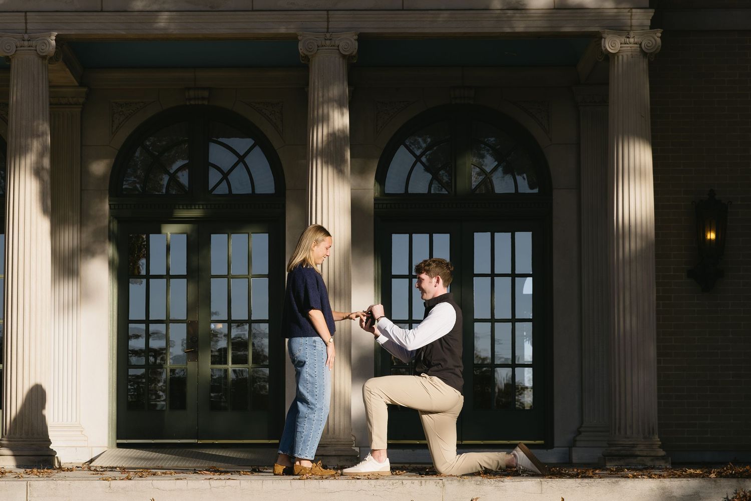 Students walk through the columned entrance of a historic university building with arched windows.