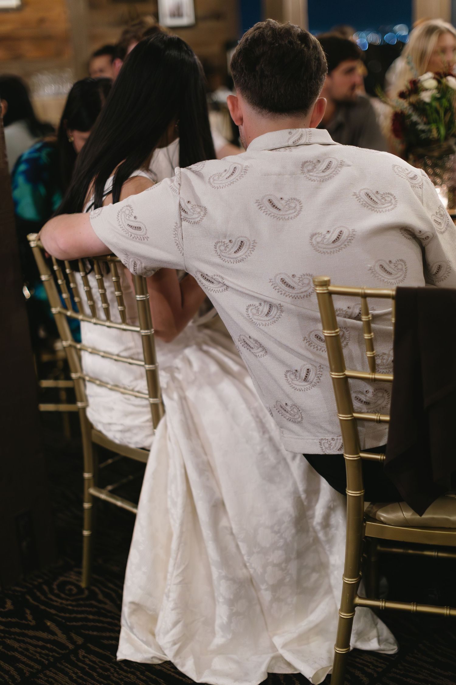 Row of white and gold chairs with matching white outfits draped over them at an indoor event.