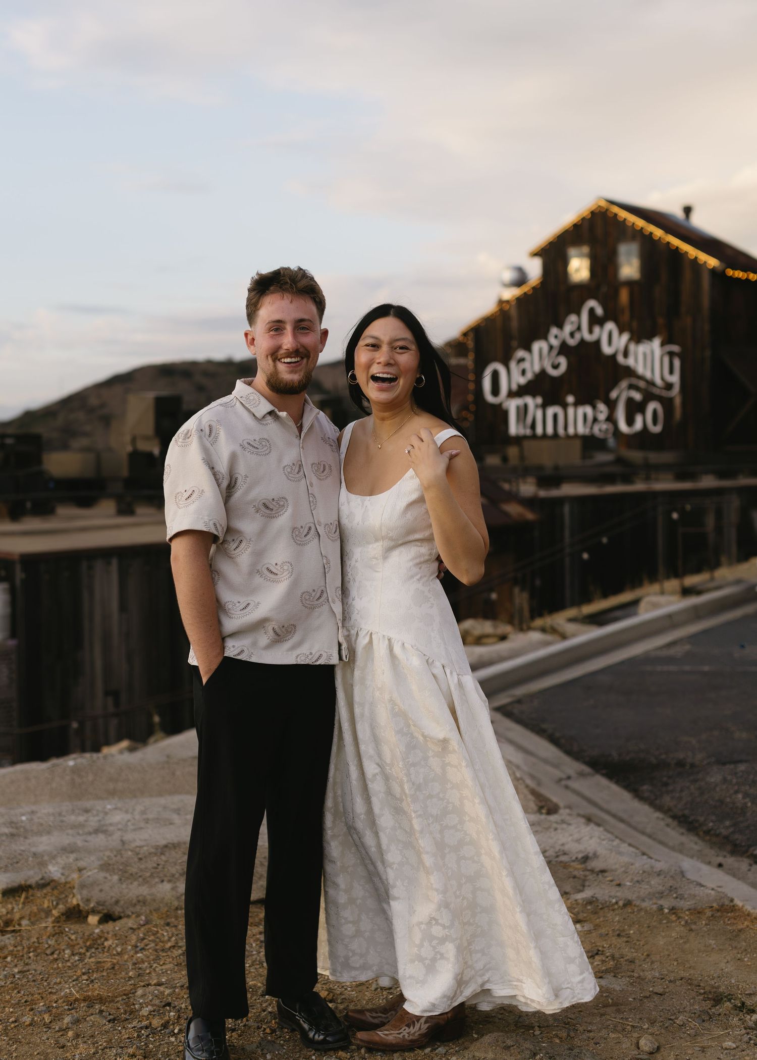 A couple poses playfully in front of rustic buildings during an engagement photo session.