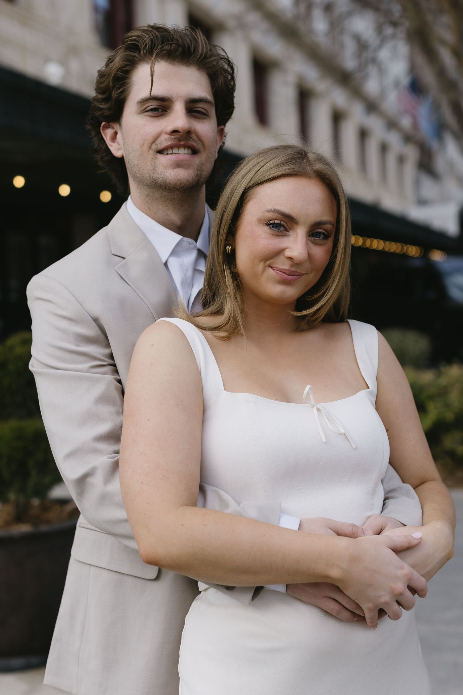 A couple embraces while wearing formal attire outdoors.