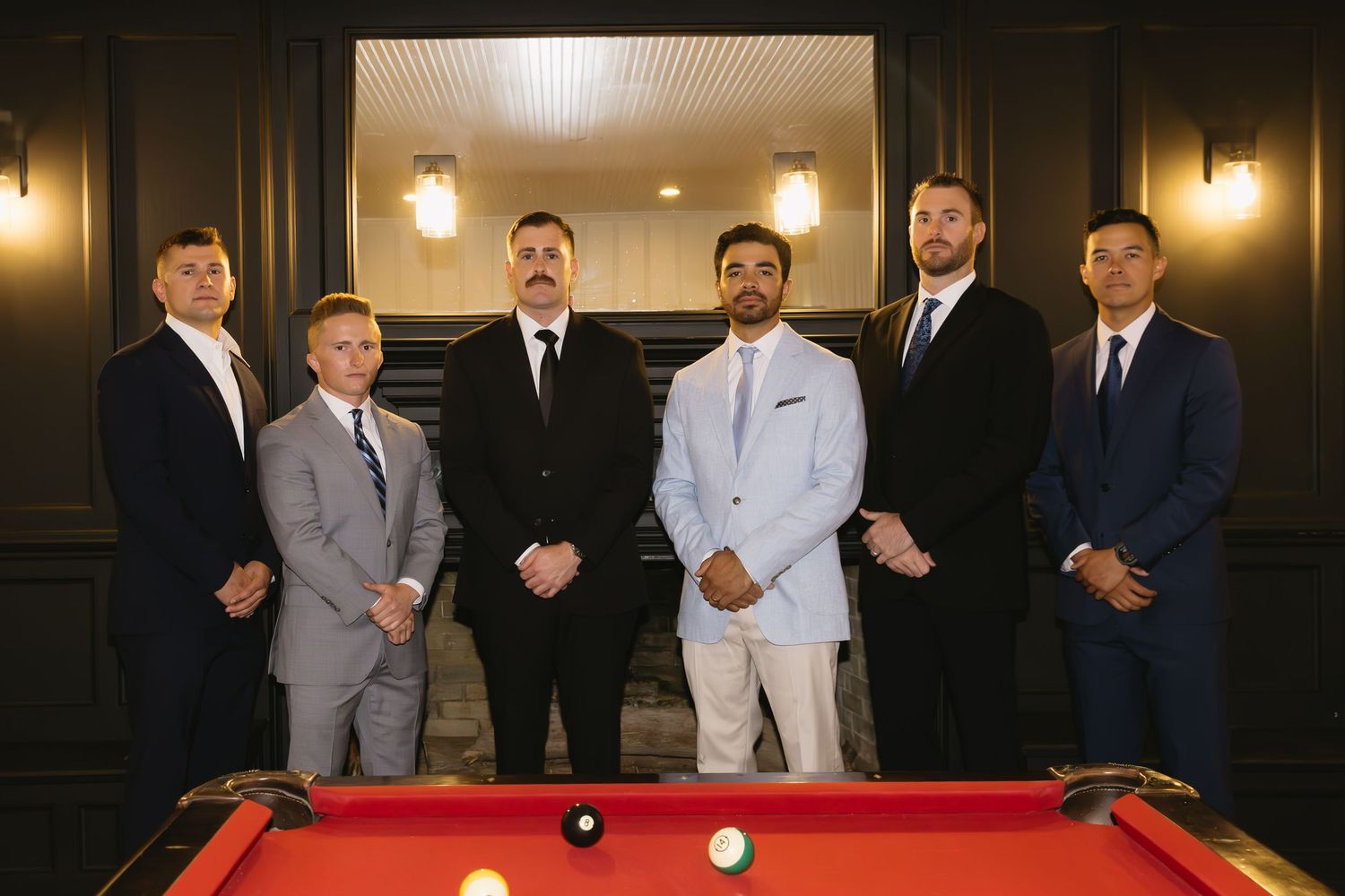 Group gathered around a red pool table in formal attire at an indoor venue.