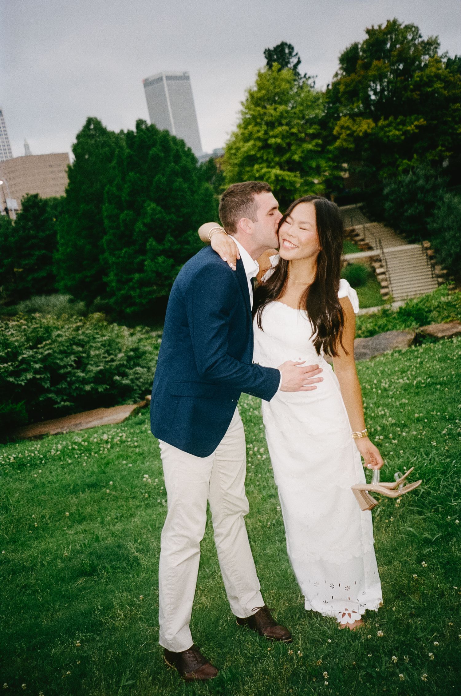 A couple embraces and shares a dip kiss on a grassy hillside during their engagement photo session on a sunny day.