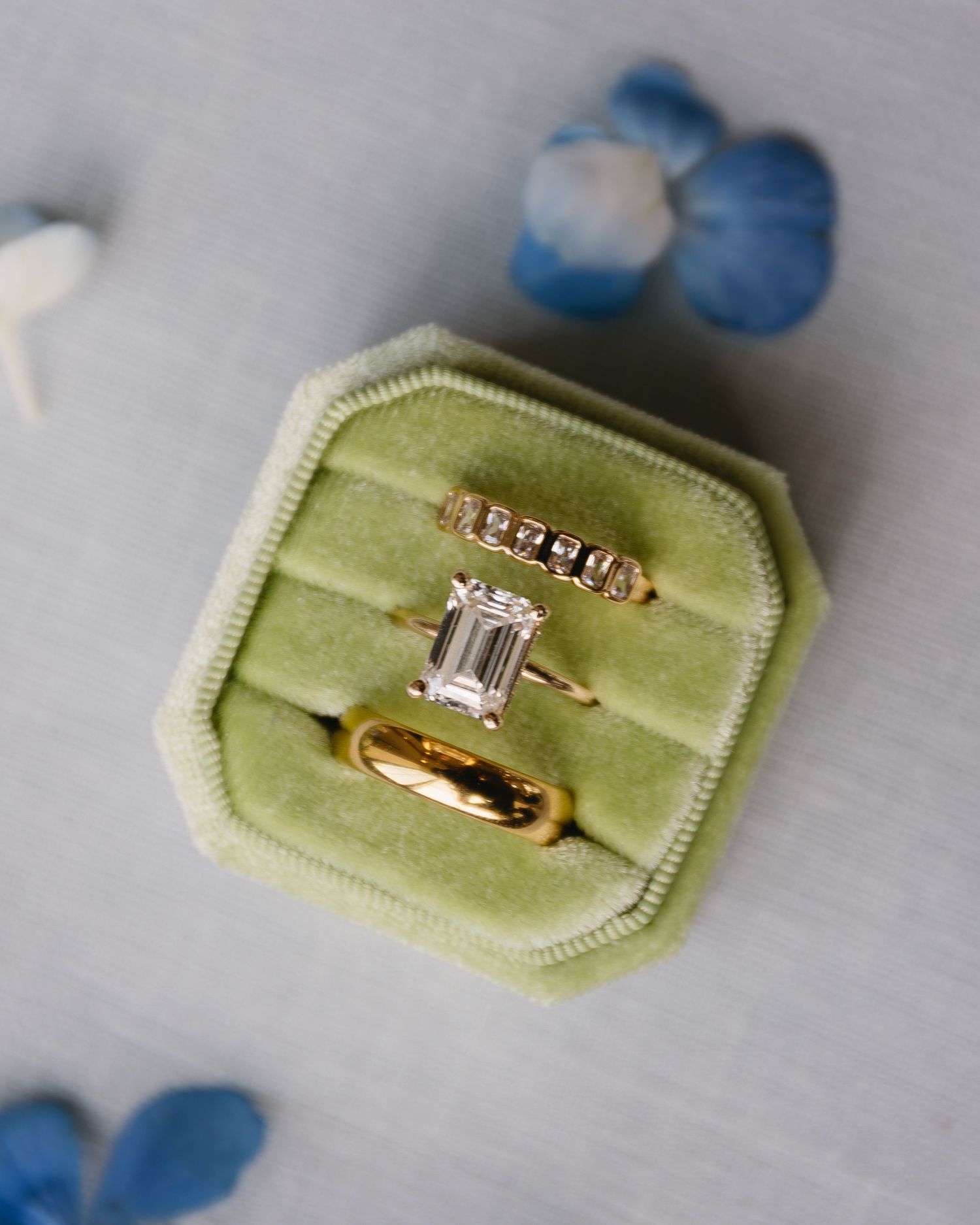 Gold engagement rings displayed on light green velvet ring boxes with blue floral accents.
